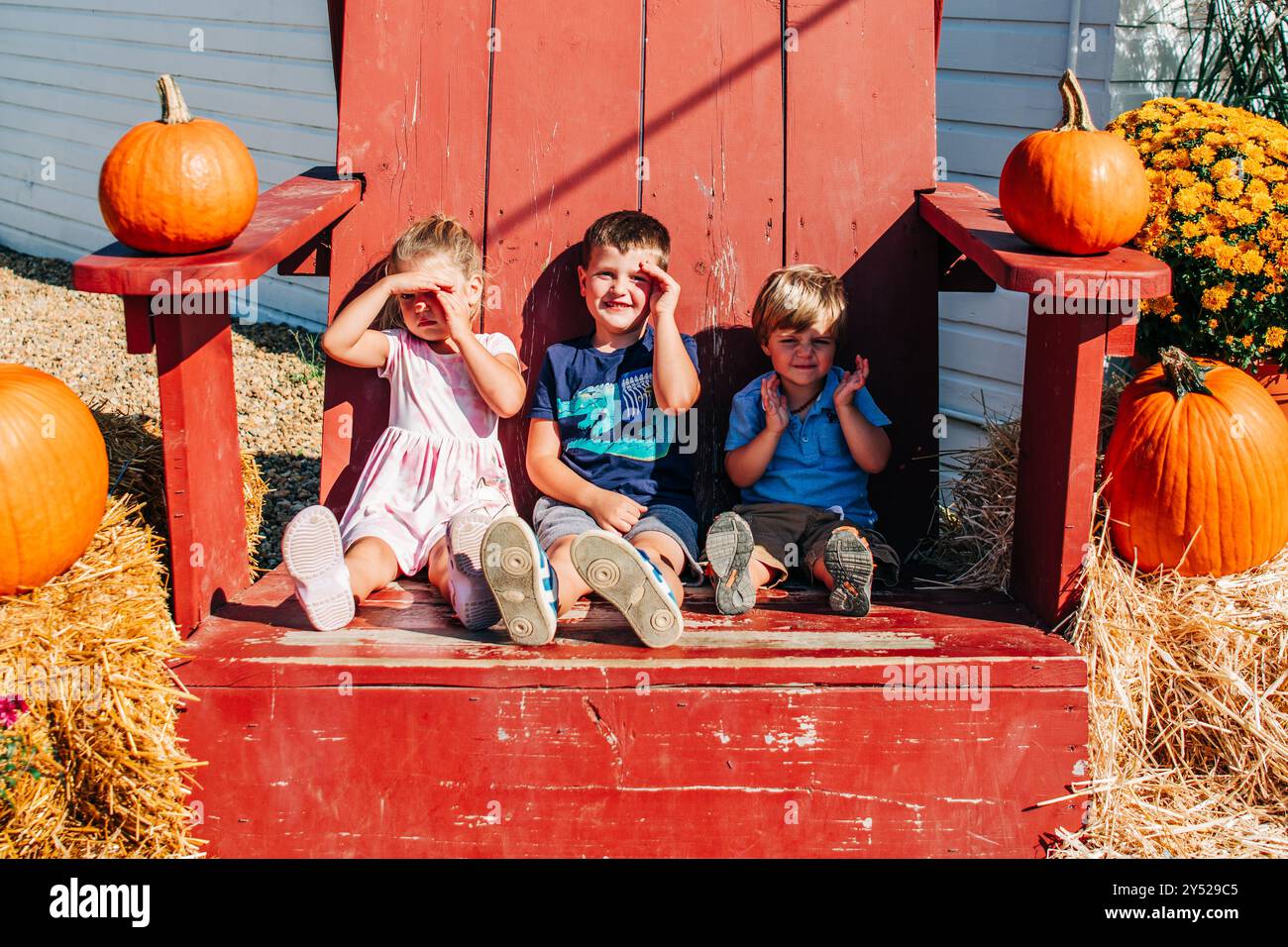 Three kids sitting on a large red chair, surrounded by pumpkins Stock Photo