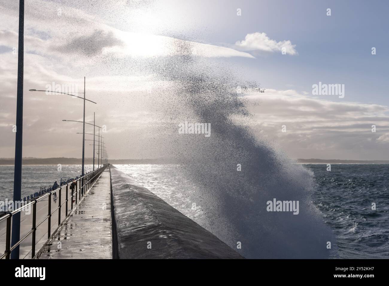Dramatic waves crashing against a pier under a bright sky Stock Photo