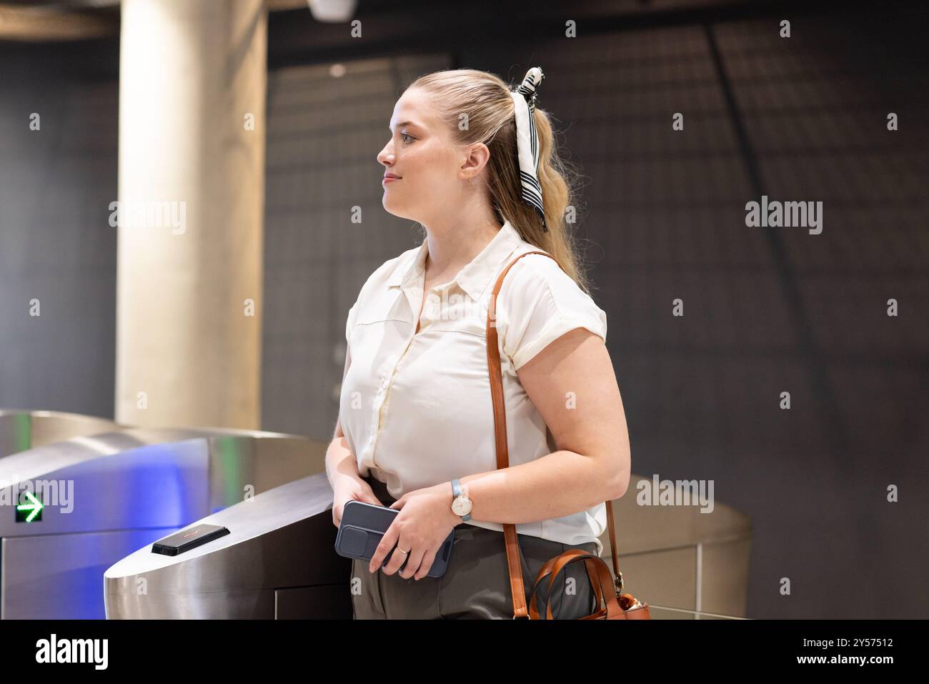 Holding smartphone, woman waiting at office turnstile in business attire Stock Photo