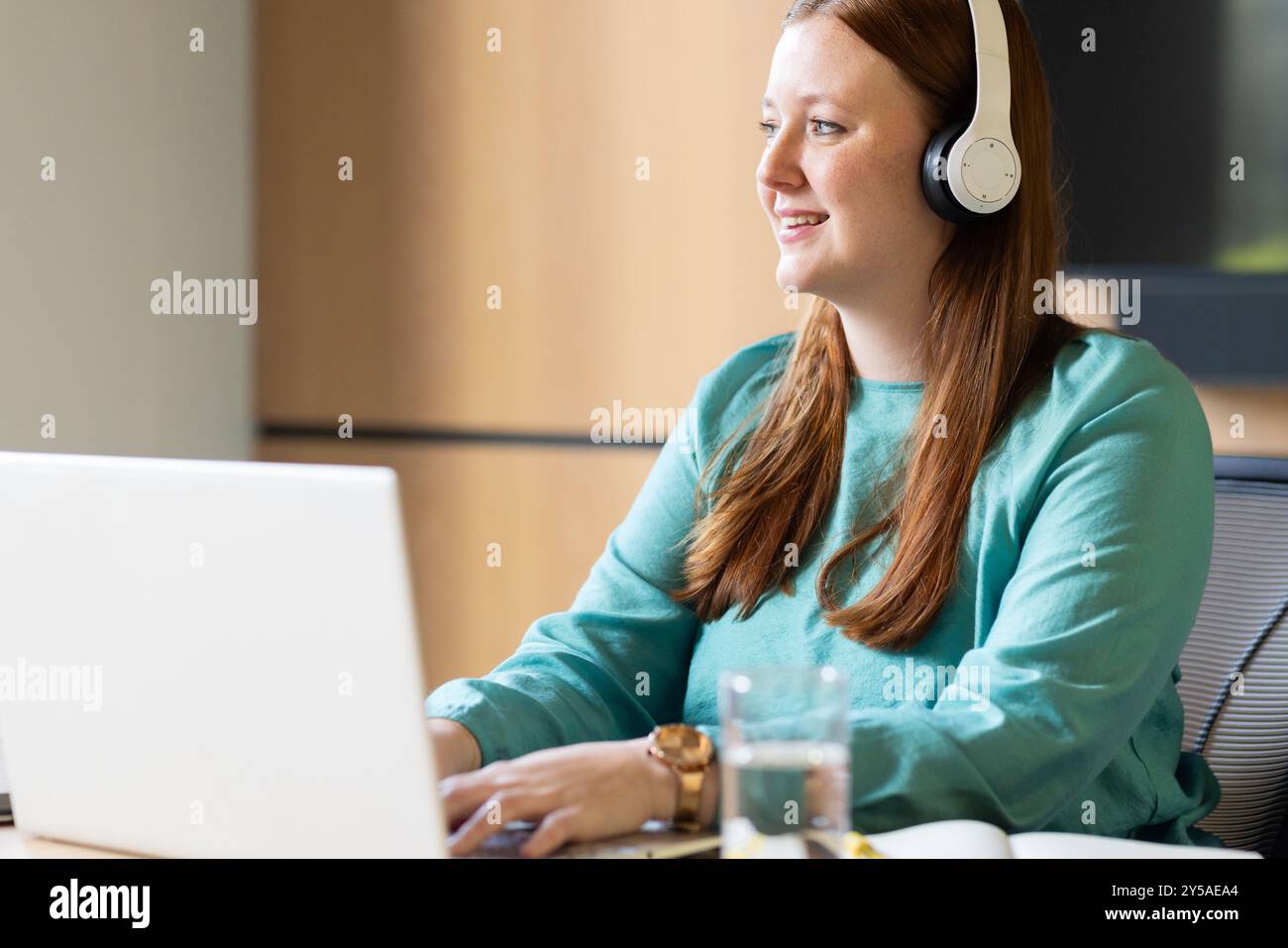 Using laptop and wearing headphones, woman working at office desk Stock ...