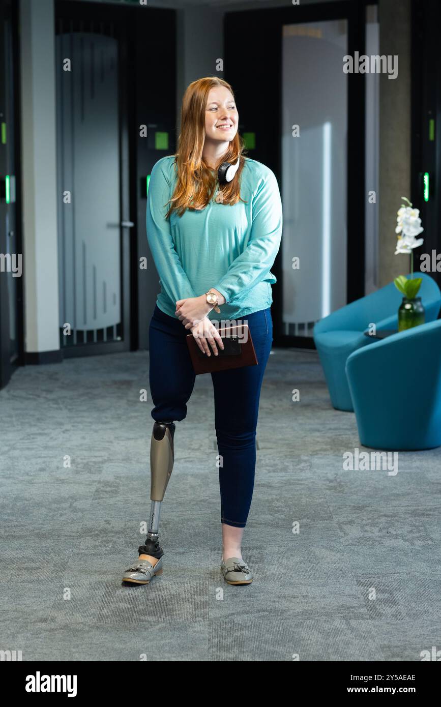 Smiling woman with prosthetic leg holding tablet in modern office hallway Stock Photo