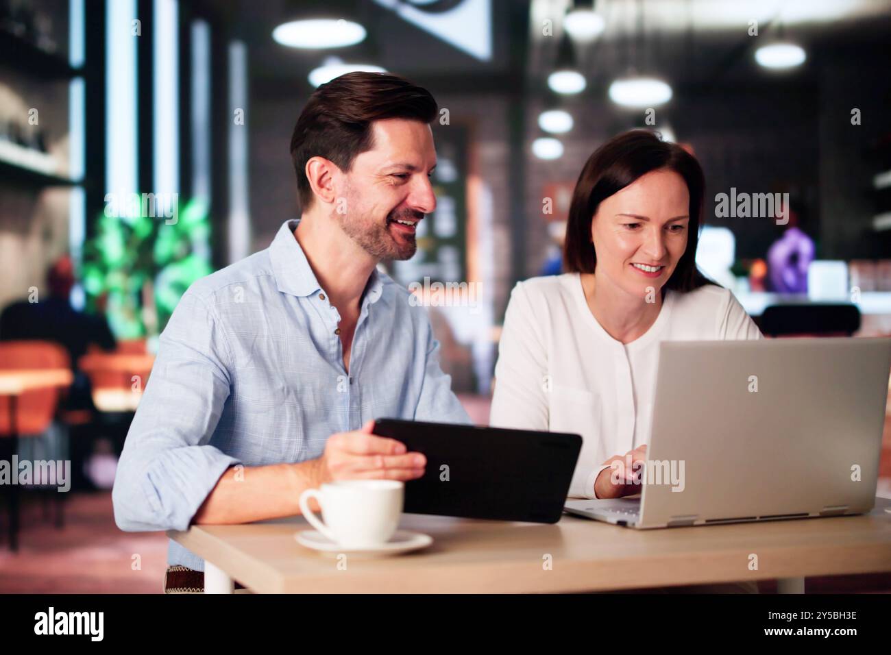 Coworkers Using Technology Lifestyle. Man And Woman Drinking Coffee In Cafe Stock Photo