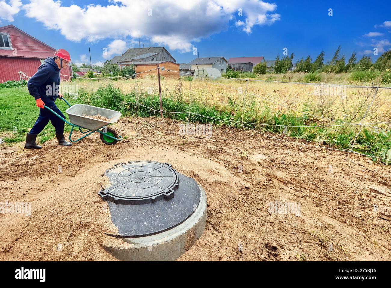 Installing wastewater plumbing for country house, worker uses wheelbarrow to transport sand. Stock Photo
