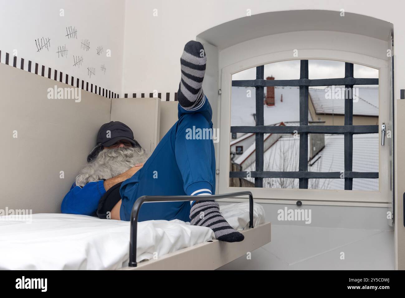 A man with a beard is sleep on a bunk bed in a prison cell Stock Photo