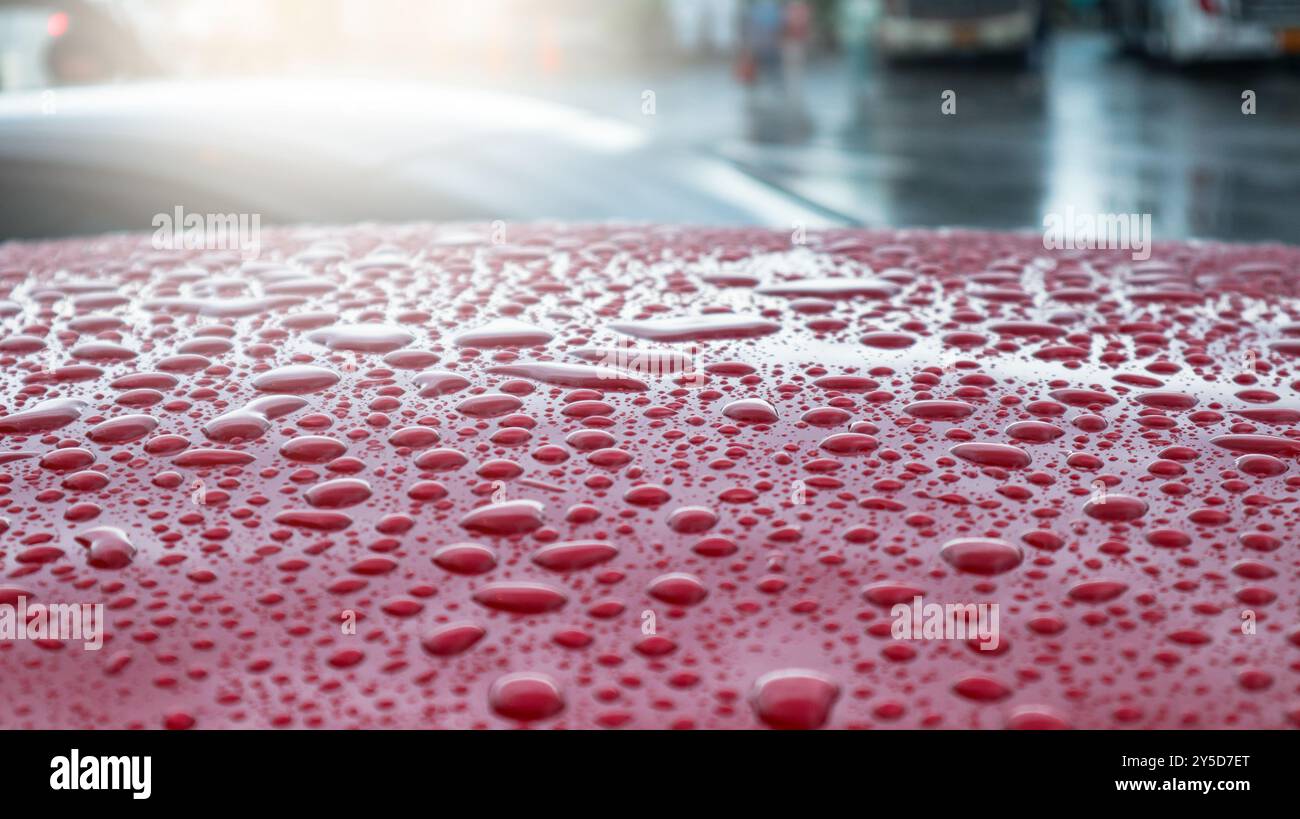 Raindrops delicately resting on the surface of a red car roof during the rainy season, reflecting the soft light and creating a serene, fresh atmosphe Stock Photo