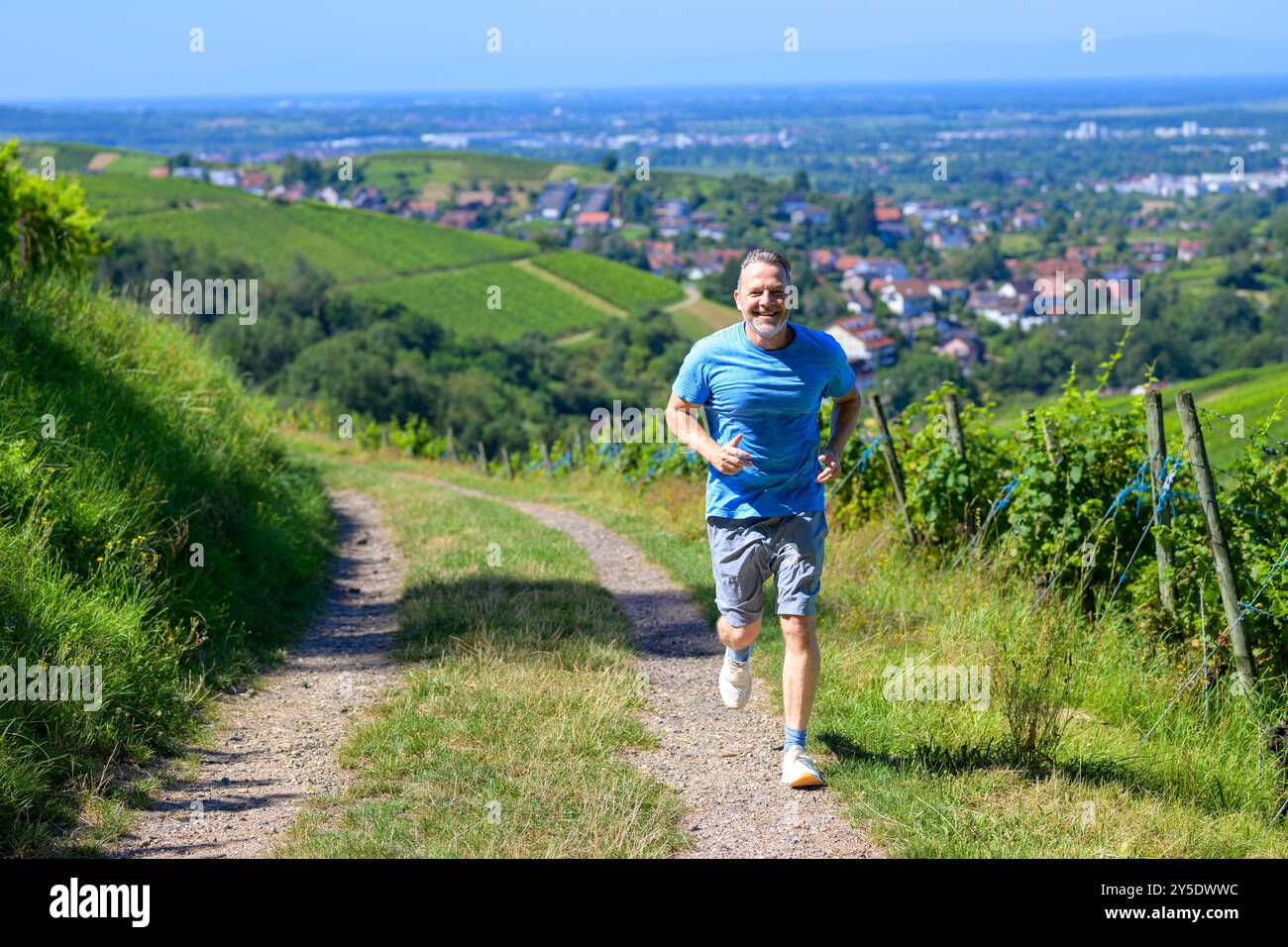 A man runs at a steady pace along a vineyard trail, smiling and energized. Stock Photo