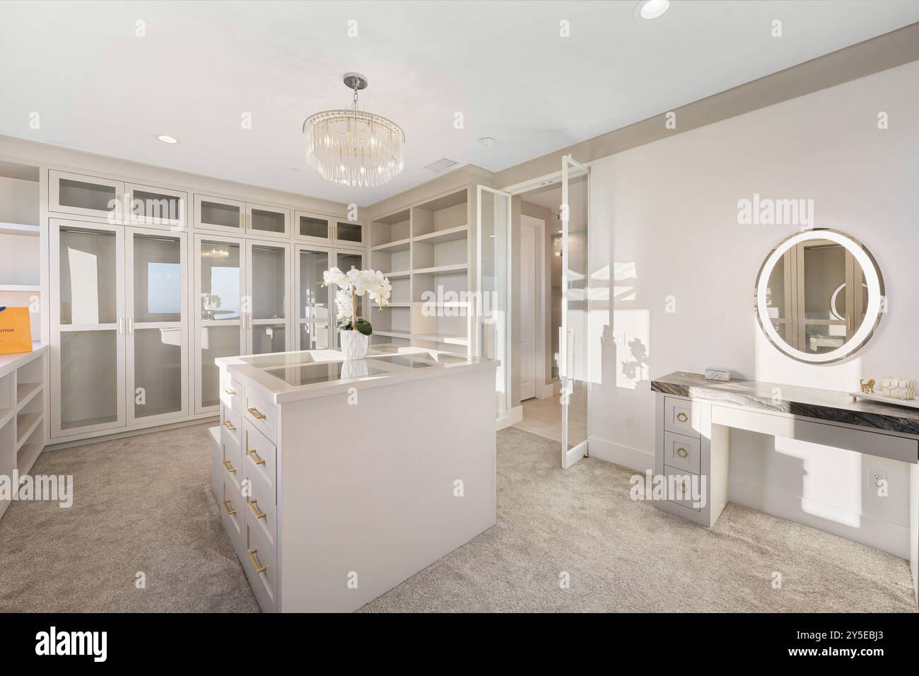 A luxurious walk-in closet with modern white cabinetry, a central ...