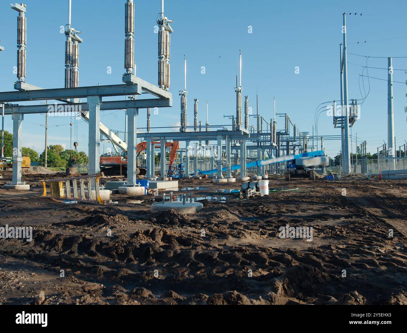 Wide view of the Electric substation under construction. Dirt piles from construction and equipment tire tracks with High Power Lines in Florida. Blue Stock Photo