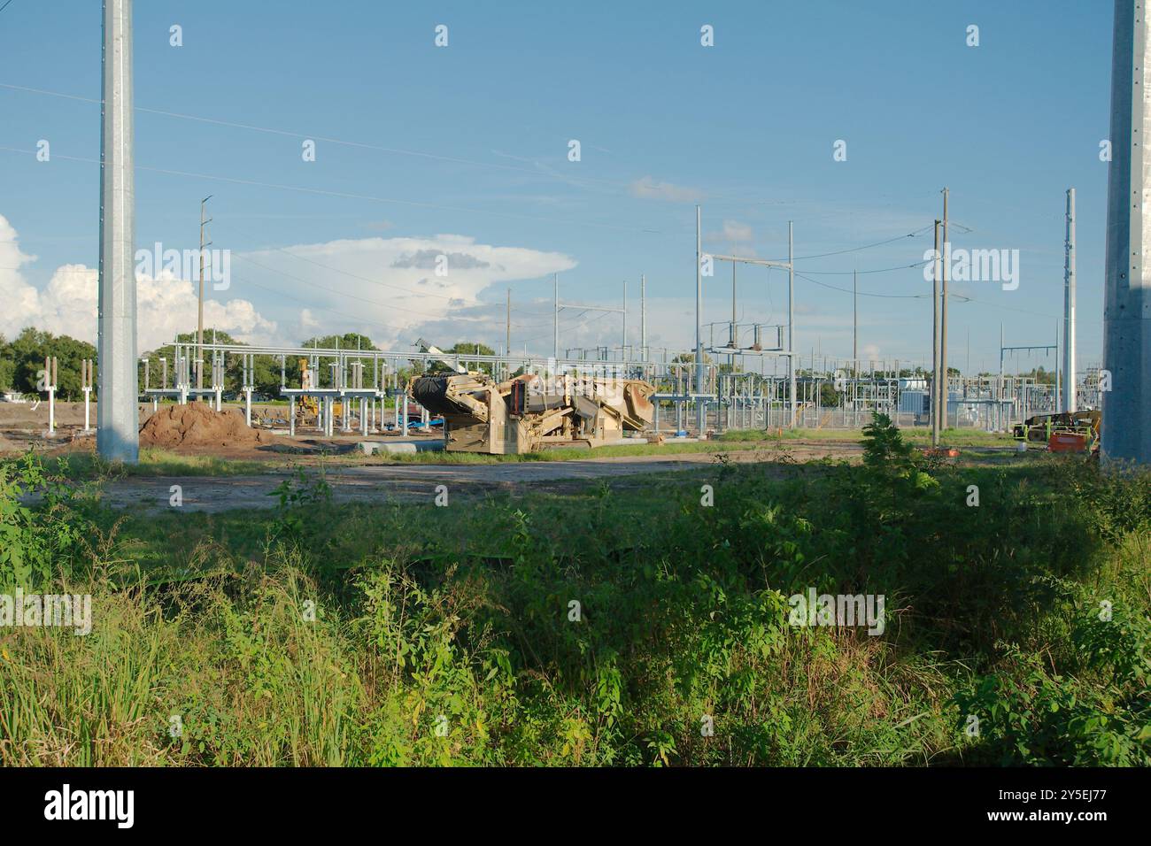 Wide view of the Electric substation under construction. Dirt piles from construction and equipment tire tracks with High Power Lines in Florida. Blue Stock Photo