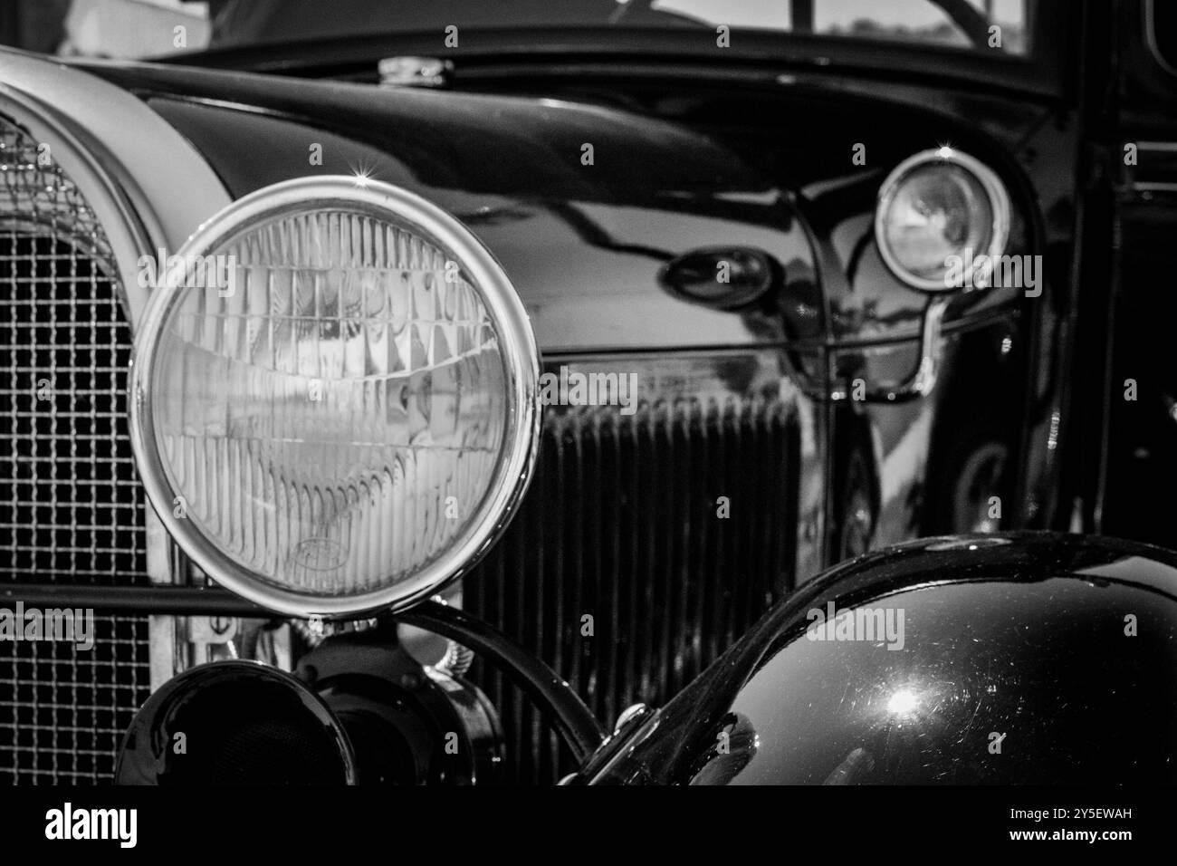 A close-up view shows the front of a vintage Ford Model A car, highlighting its prominent headlight and gleaming grille. Stock Photo