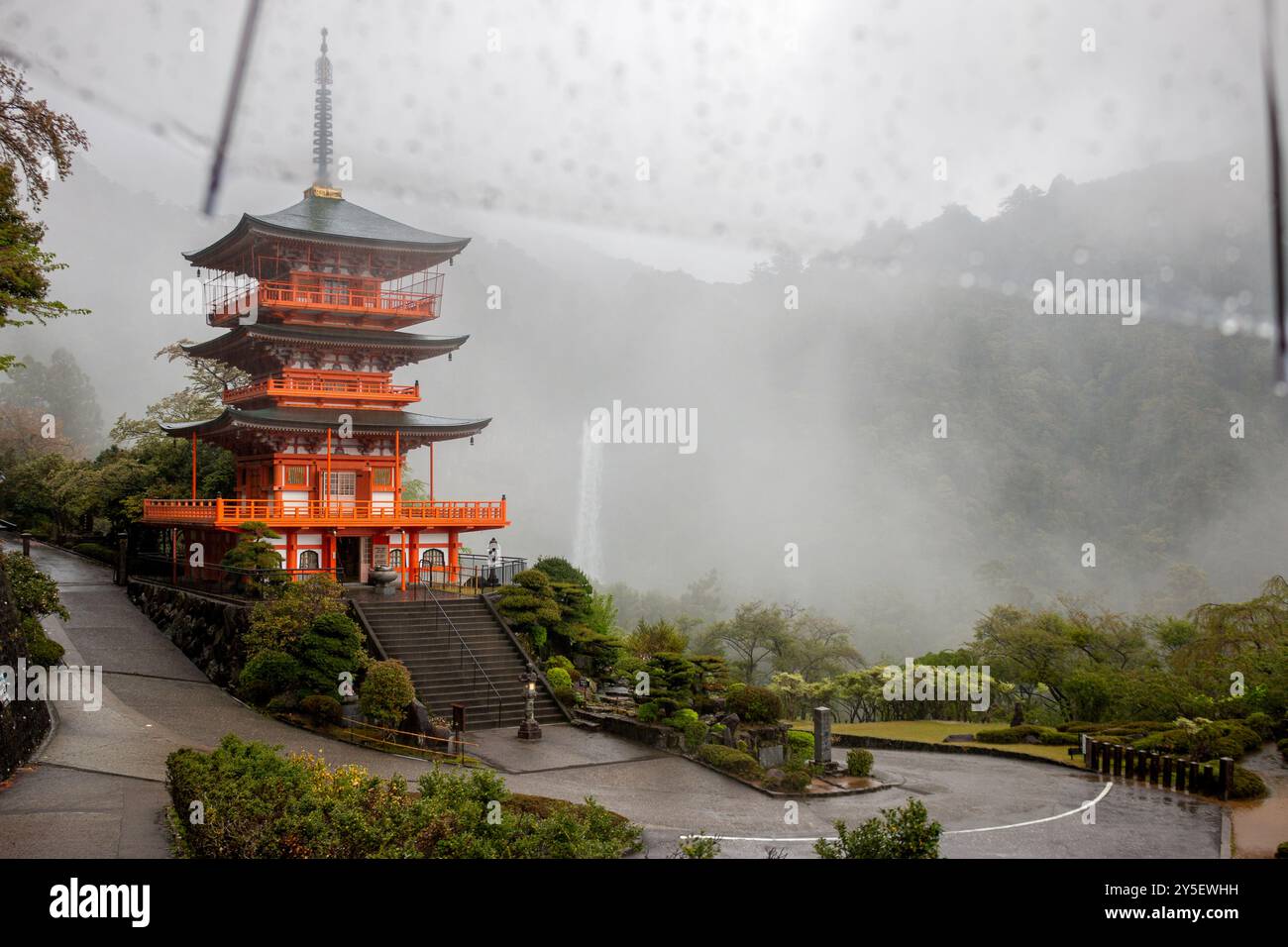 Nachisan Seiganto-ji Temple’s 3-storied pagoda with Nachi Falls behind in the rain from underneath an umbrella, April, Japan Stock Photo