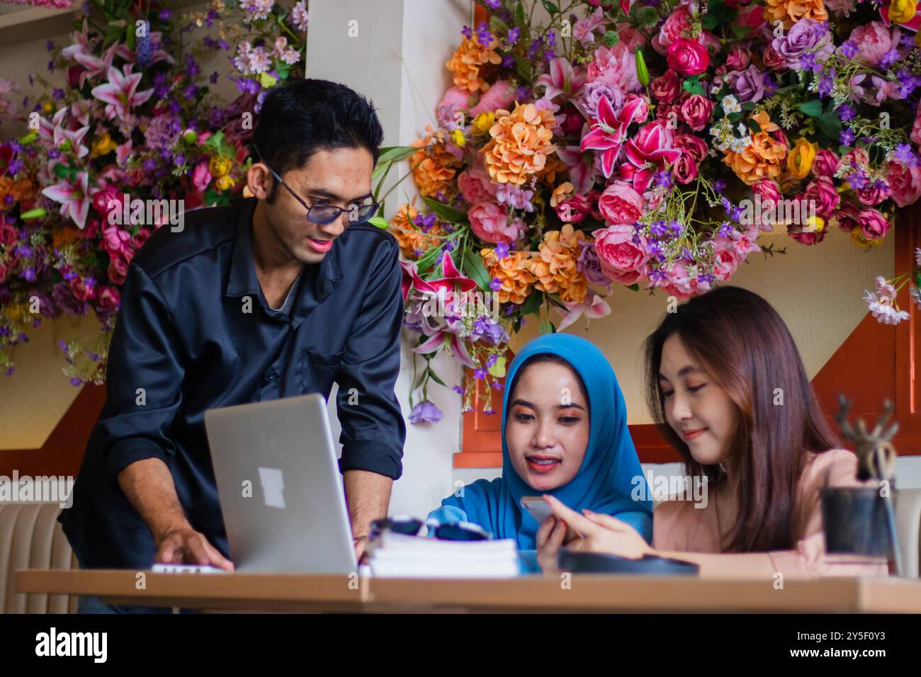 A group of Asian students listen to a presentation on a cellphone in front of a laptop from a lecturer in a coffee shop cafe. for group concept, compa Stock Photo