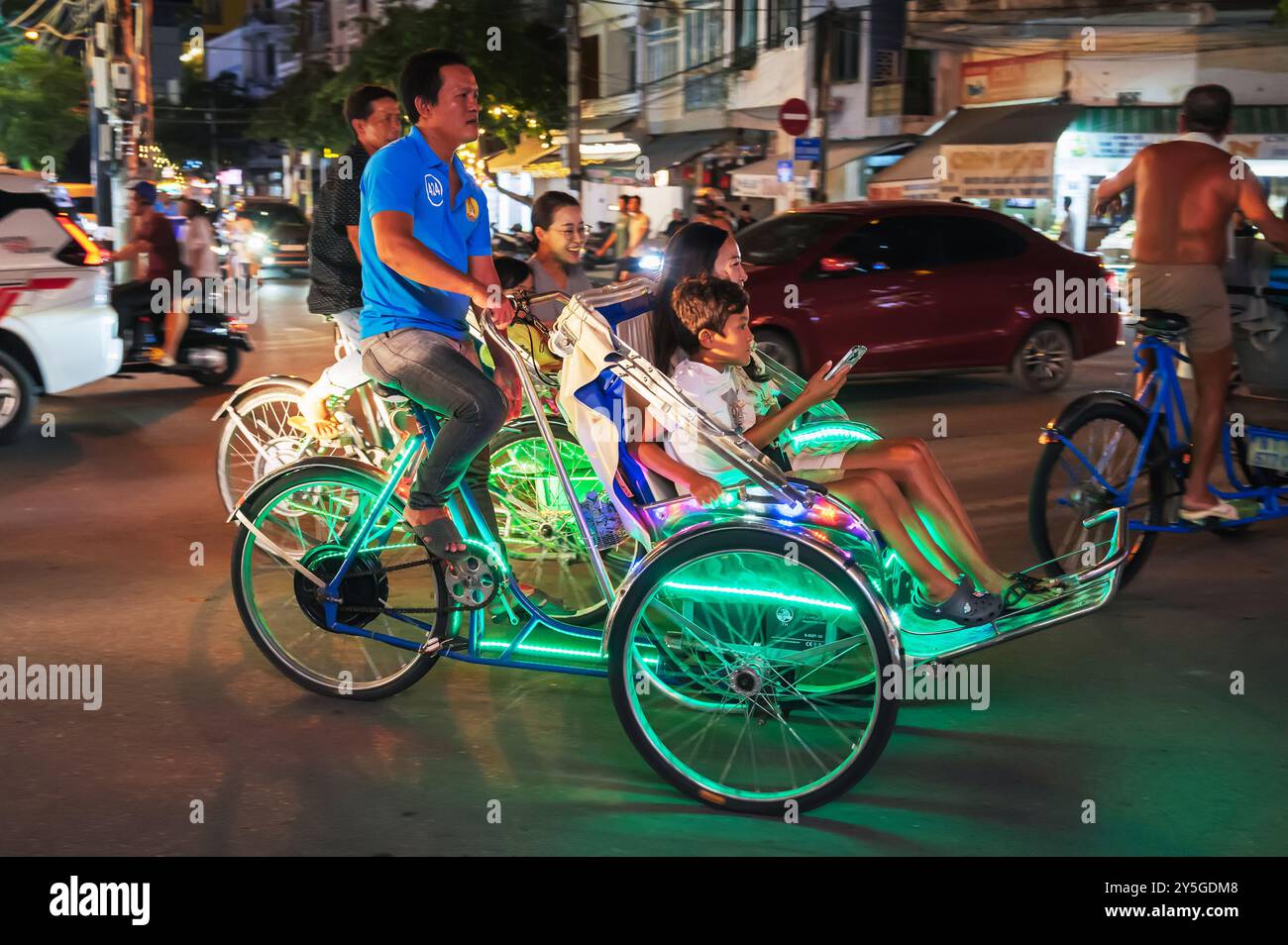 A bicycle rickshaw takes tourists along the road in the night city. Nha ...
