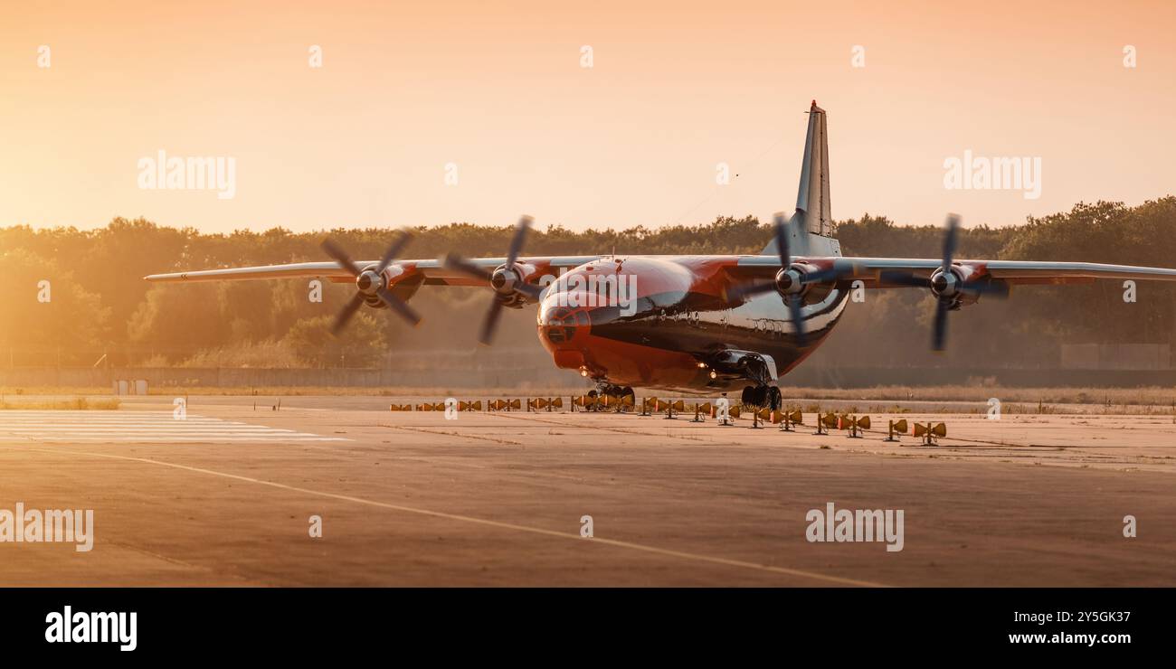 Orange turboprop aircraft preparing for takeoff at sunset. Front three quarter view of cargo aircraft with four propellers spinning. Stock Photo