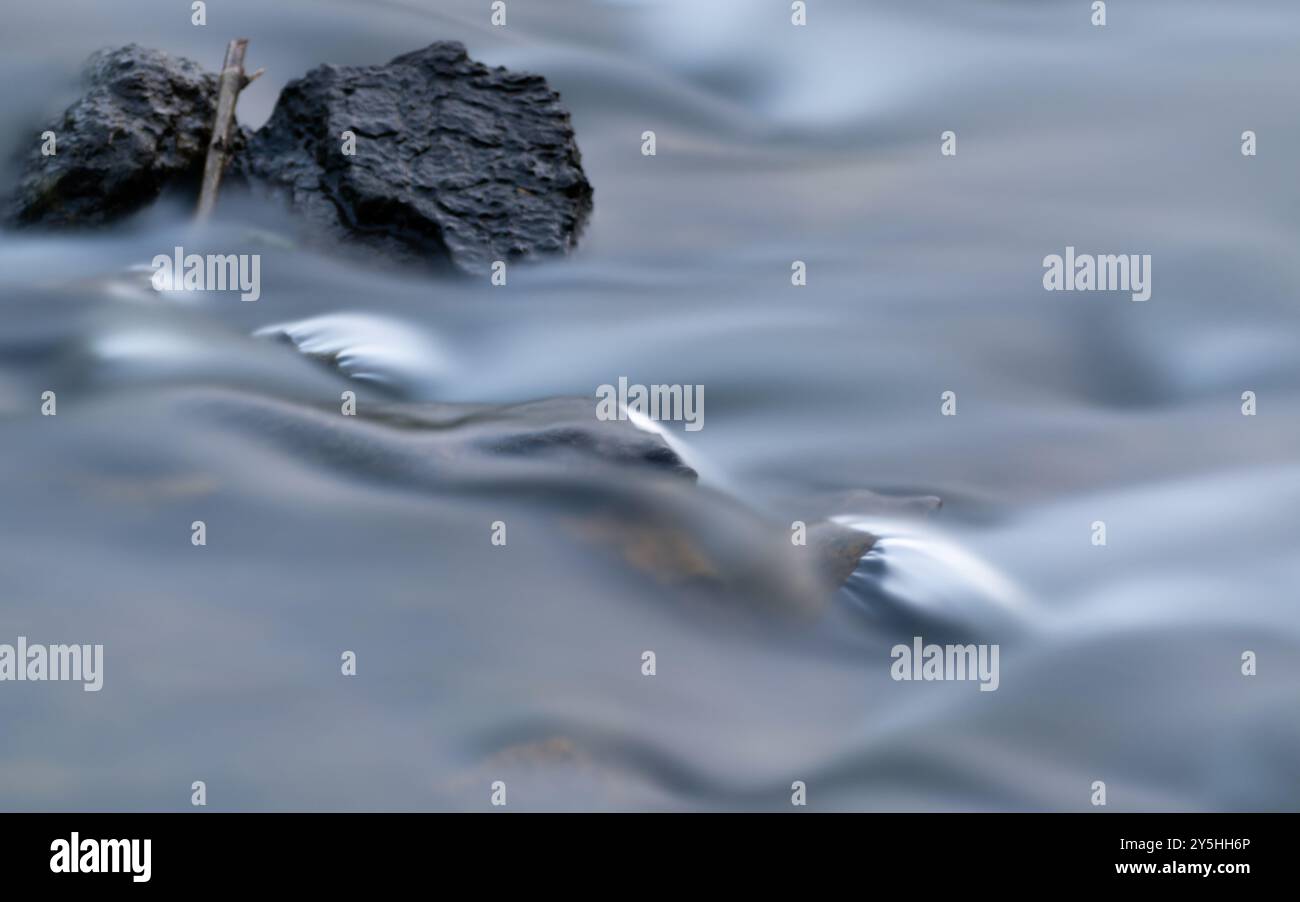 Rocks and wood in creek with silky water, long exposure Stock Photo