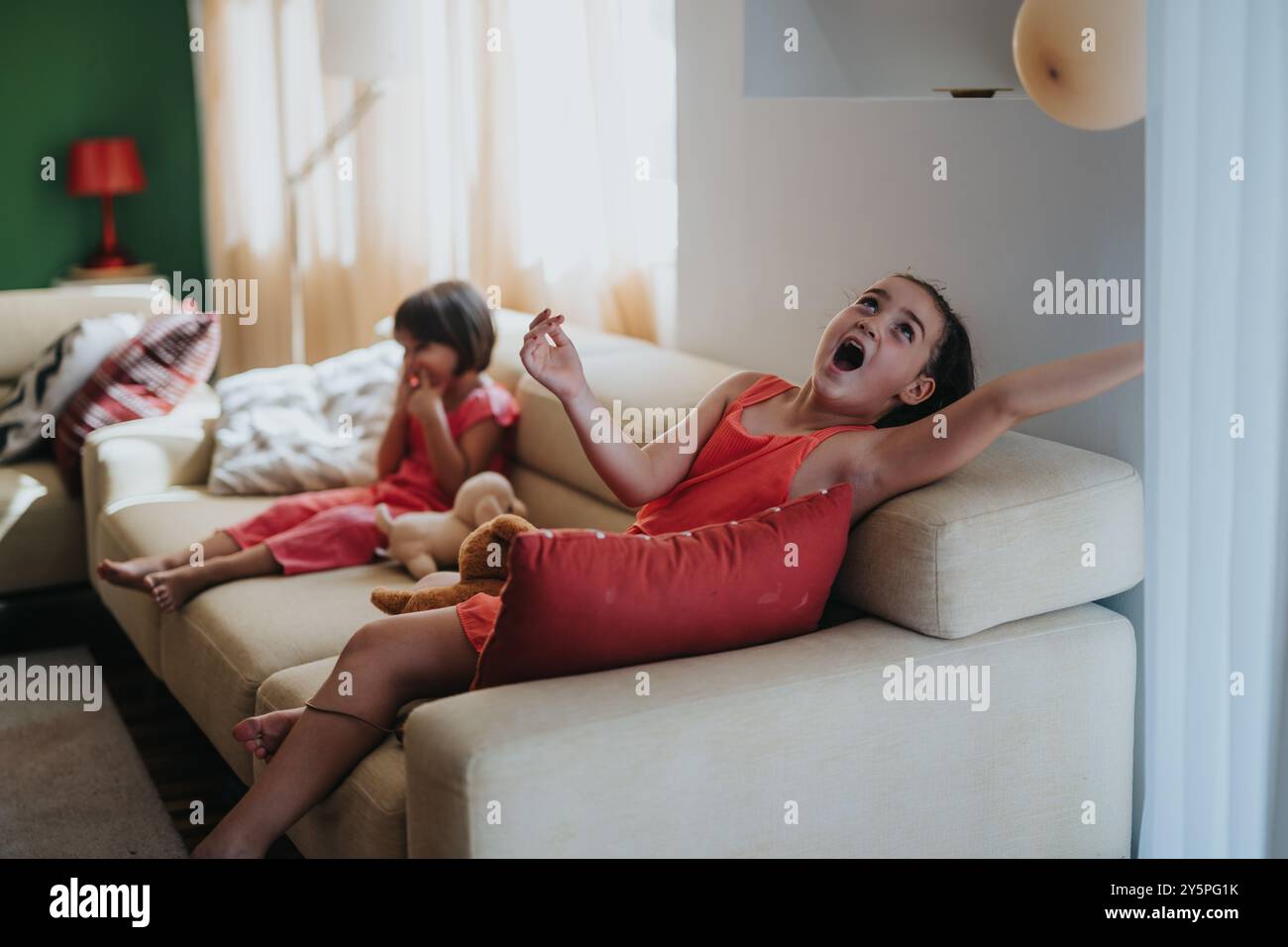 Two young girls playing joyfully on a cozy living room sofa Stock Photo ...