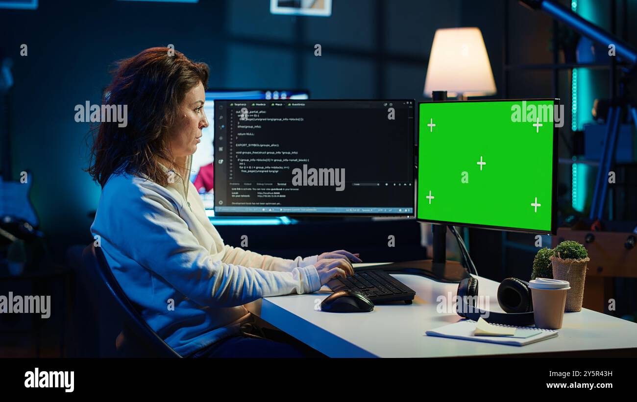 Developer doing software debugging on green screen PC at home, checking lines of code displayed on monitors. IT professional in living room fixing coding problems on mockup computer, camera A Stock Photo