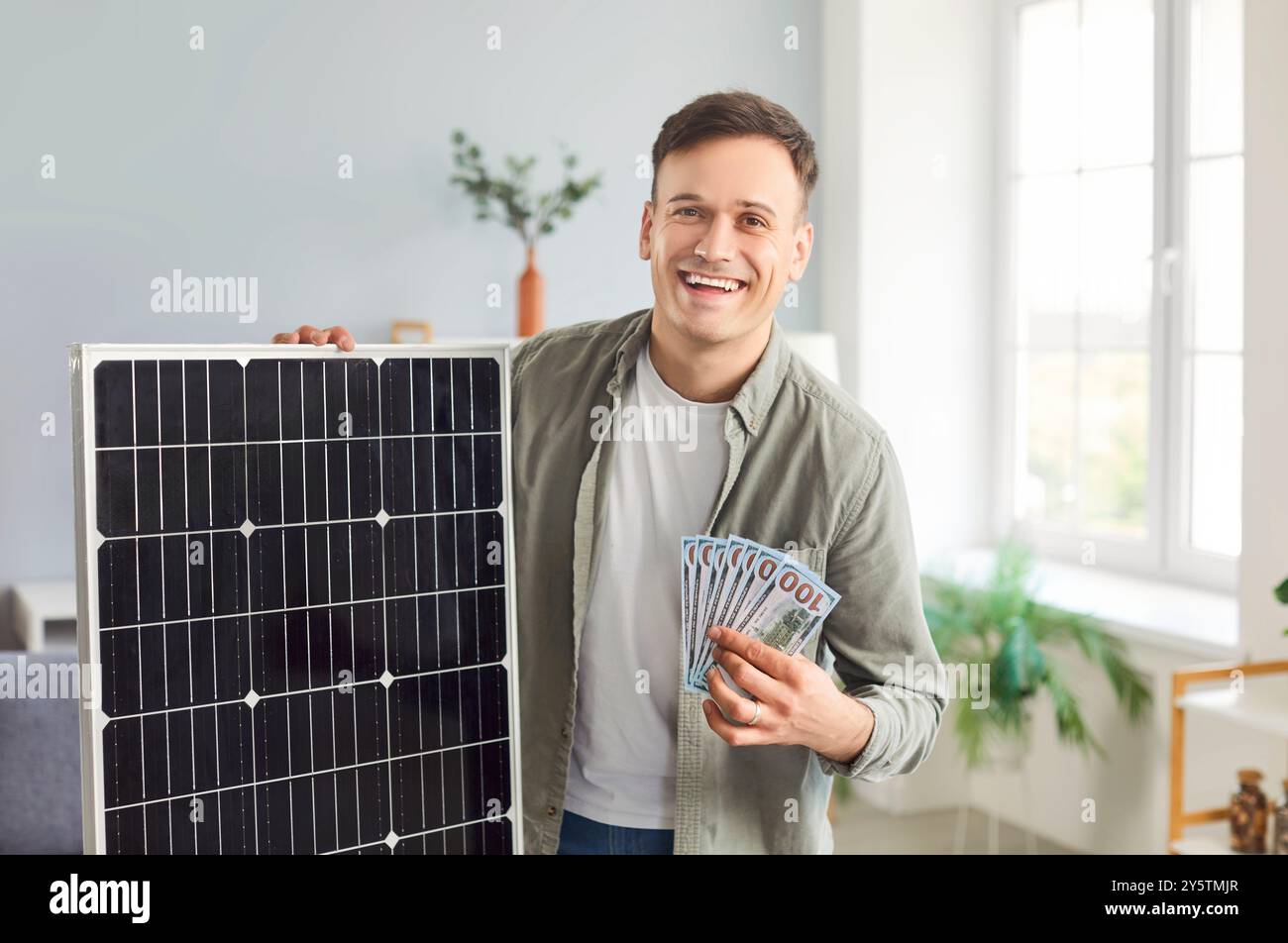 Happy man holding a photovoltaic solar panel and showing money that he saved while using it Stock Photo