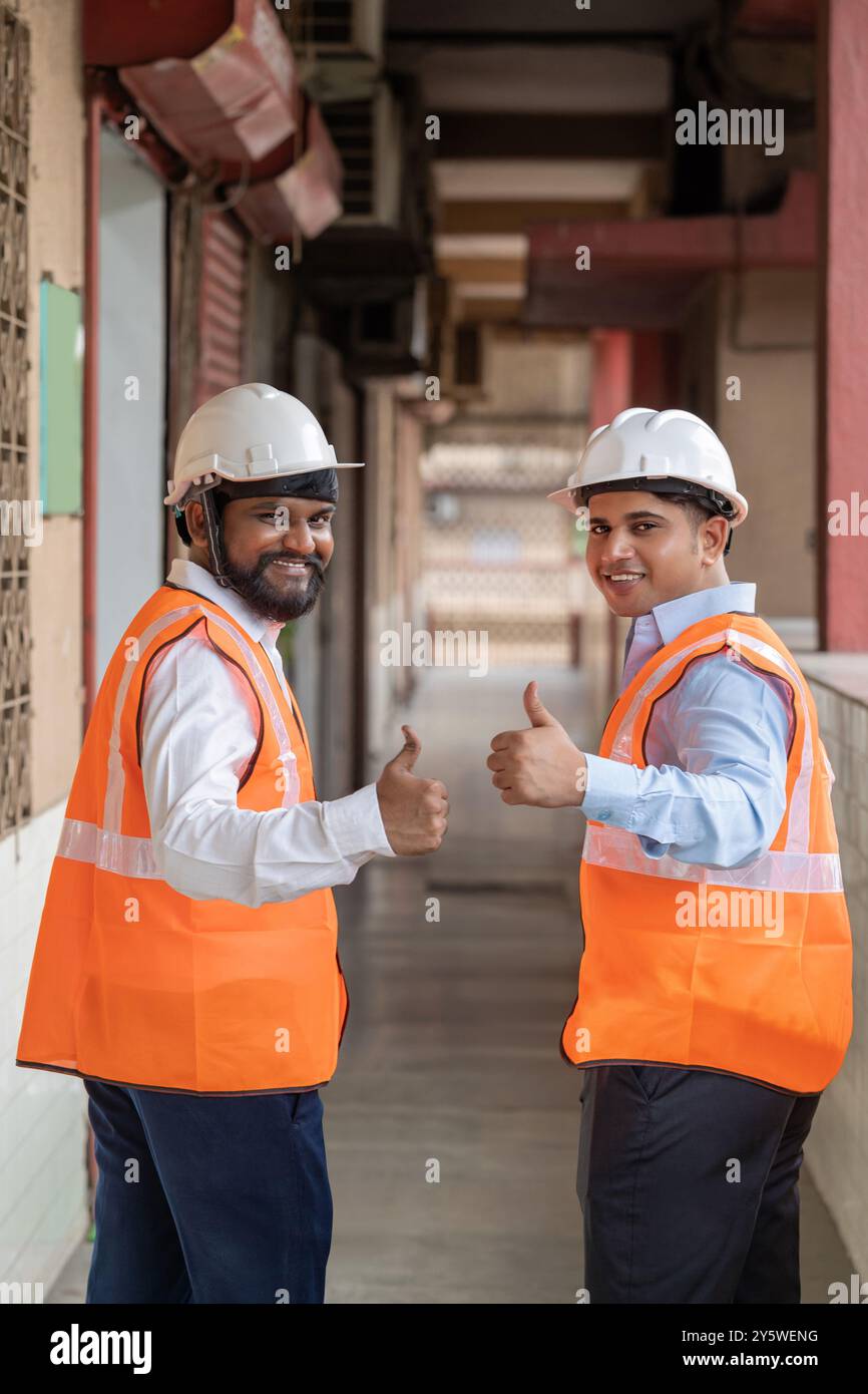 Two warehouse construction workers in a commercial industrial warehouse setting, both giving a thumbs-up and their positive expressions and confident Stock Photo