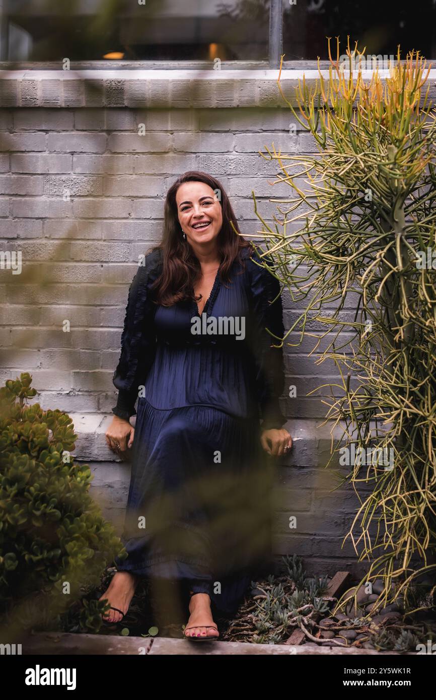 Happy woman sitting in front of a grey brick wall. Stock Photo