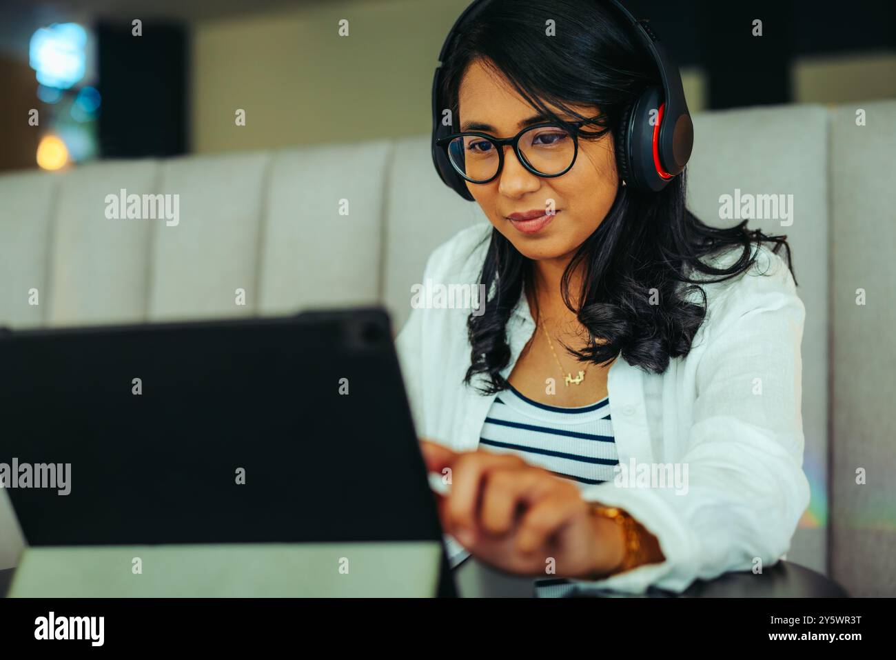 Engaged student using headphones while learning on a tablet in a cozy setting. The image captures focused study and a modern educational experience. Stock Photo