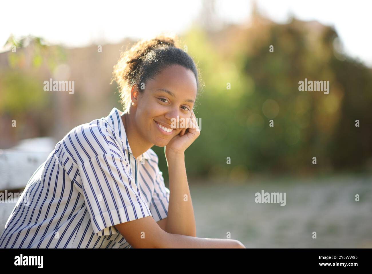 Happy black woman looks at camera posing sitting in a park Stock Photo ...