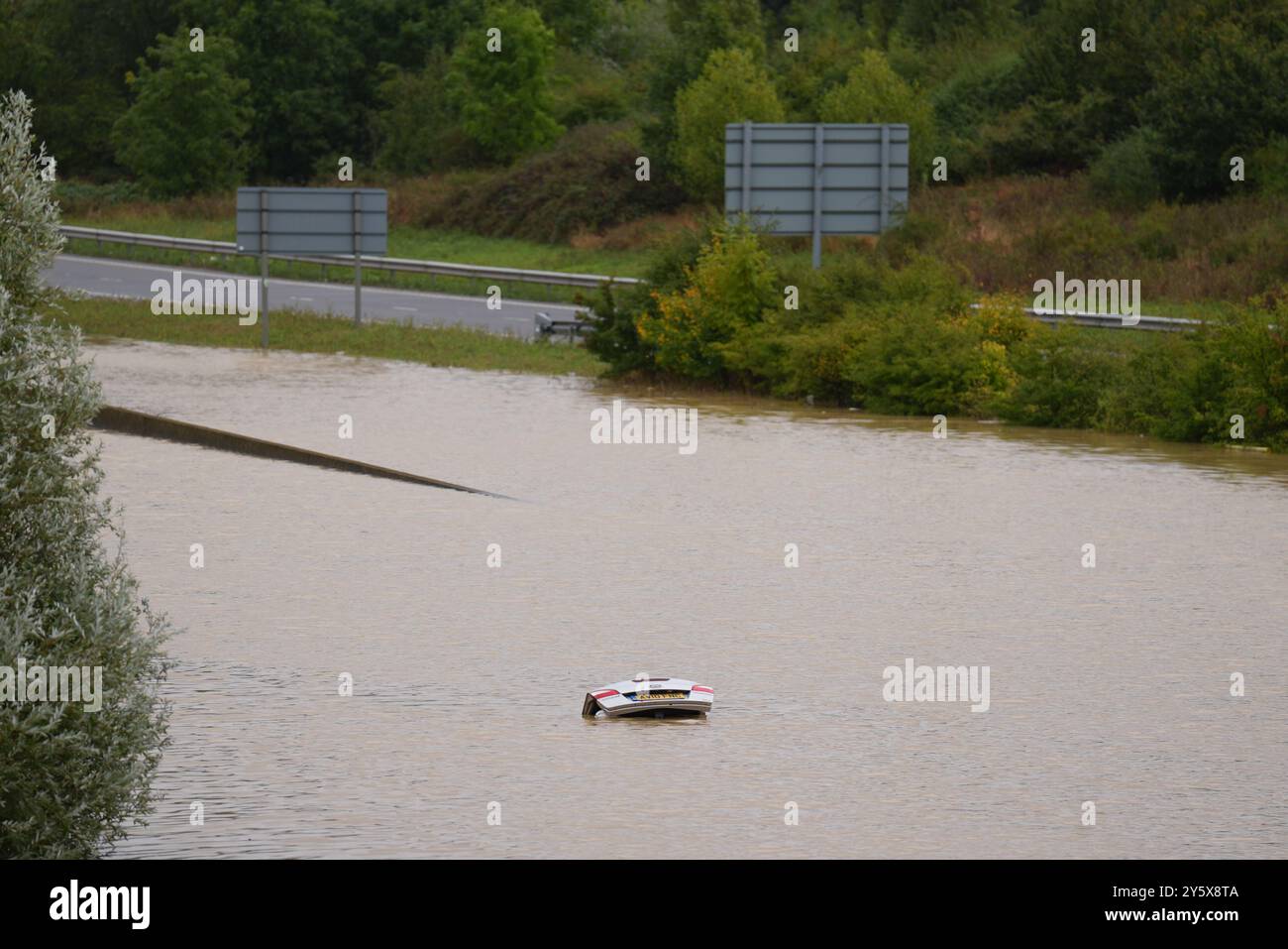 The open boot of a car is visible above the water where the vehicle is submerged in flood water on the A421 in Marston Moretaine, Bedfordshire. Parts of Britain have been struck by flash floods after some areas saw more than a month's worth of rain in 24 hours. Heavy rainfall has seen parts of Northamptonshire, Bedfordshire and London submerged causing widespread travel disruption and damage to properties. Picture date: Monday September 23, 2024. Stock Photo