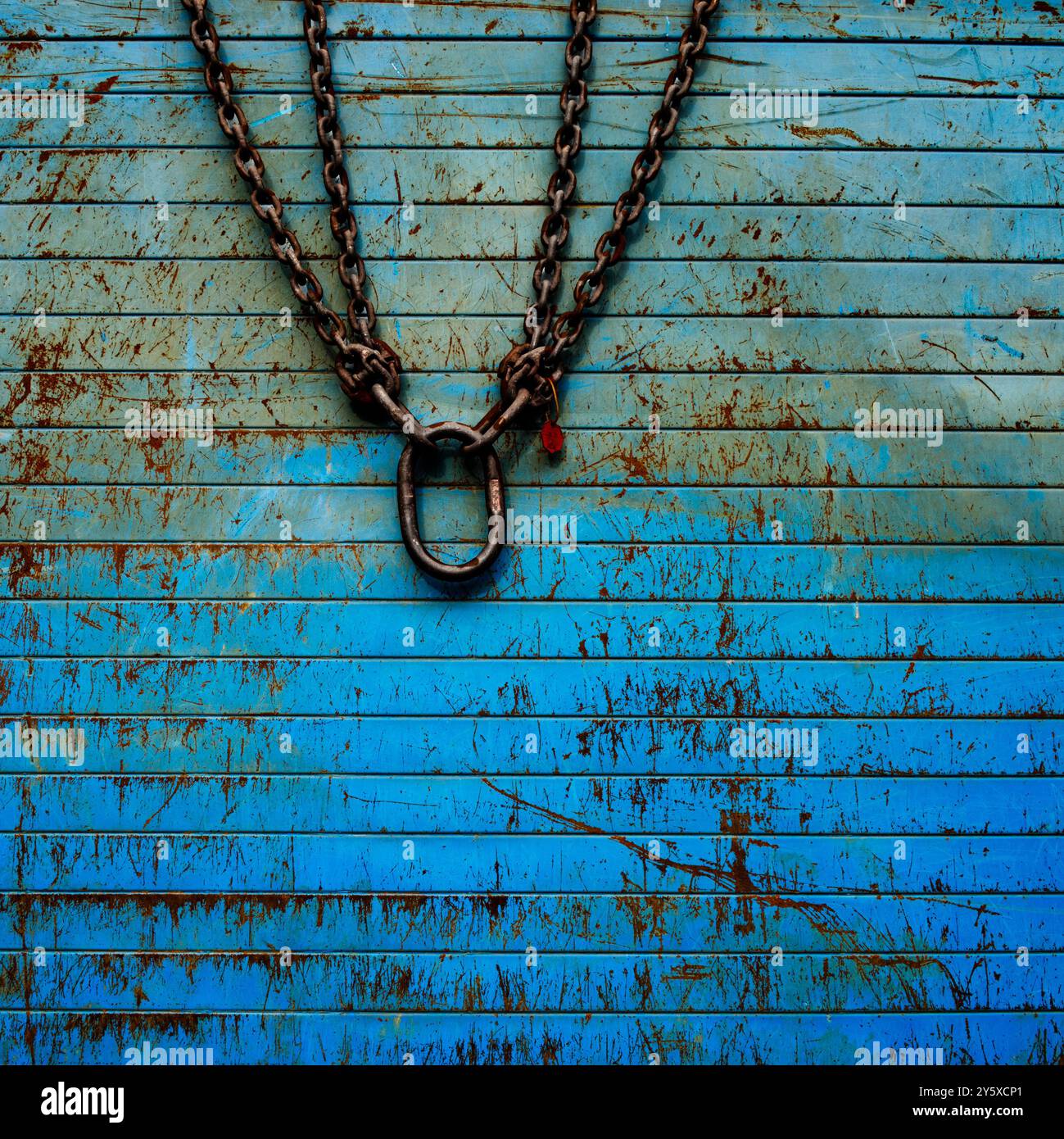 At a construction site a big heavy metal chain is hanging over a site fence with a scratchy surface in vivid blue colors Stock Photo