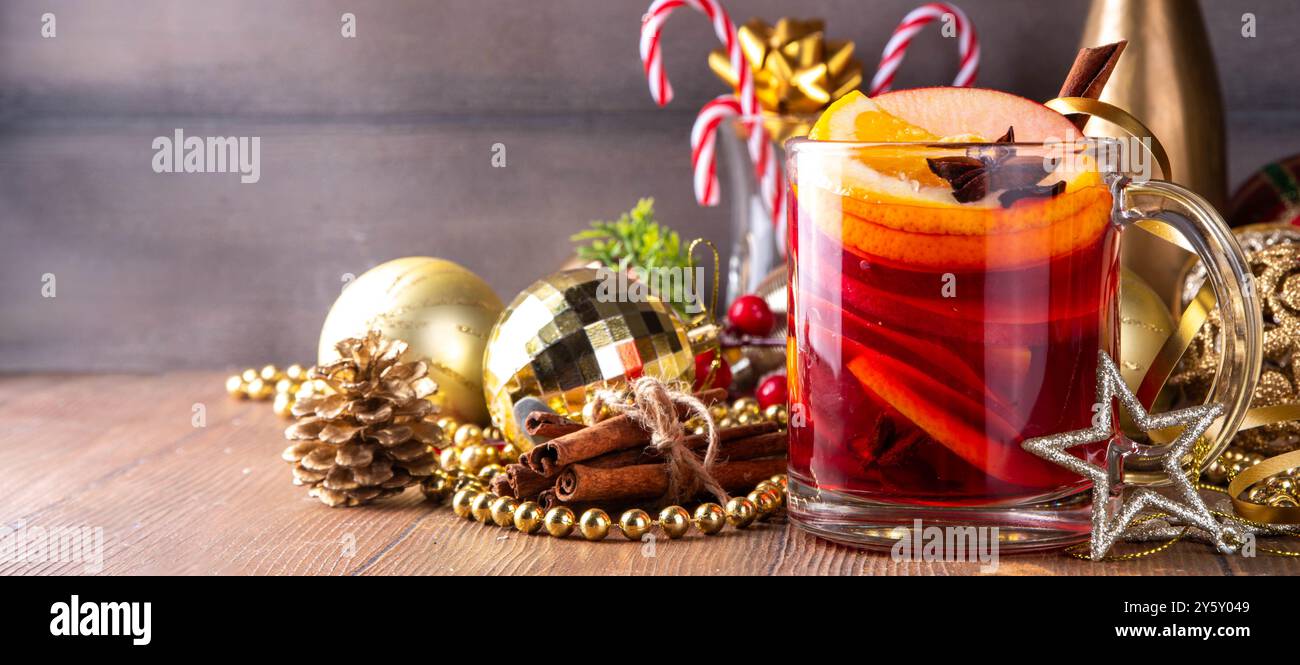 Mulled wine glass mug with sweet apple, orange, honey, cinnamon and anise star, on wooden table with Christmas decoration, holiday cozy comfort drink. Stock Photo