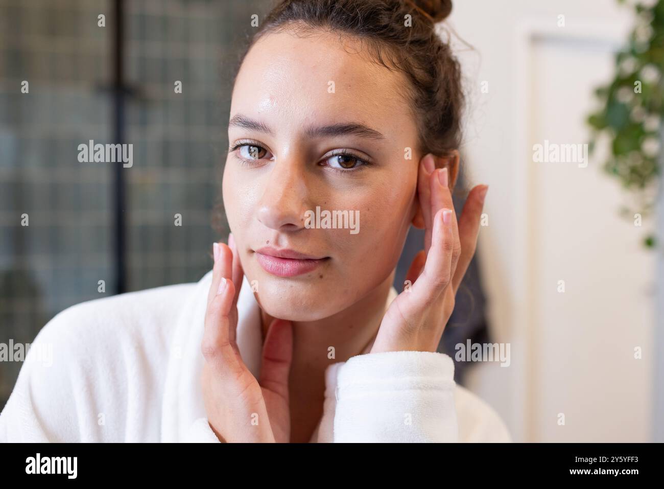 Applying skincare, woman in white robe touching face, enjoying spa ...