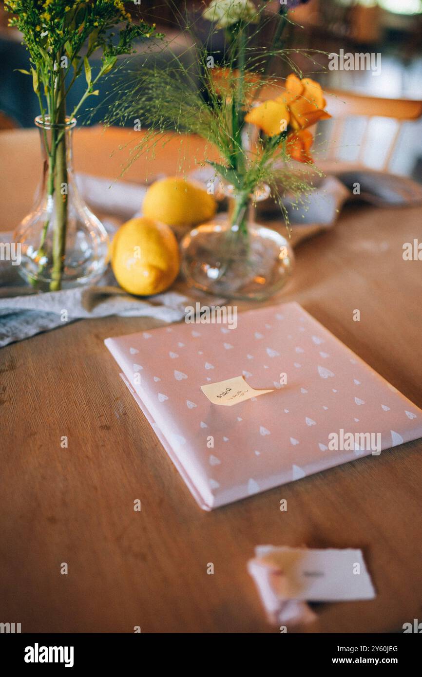 Gift Wrapped in Pink Paper with Lemons and Floral Vase Decor on Wooden Table Stock Photo
