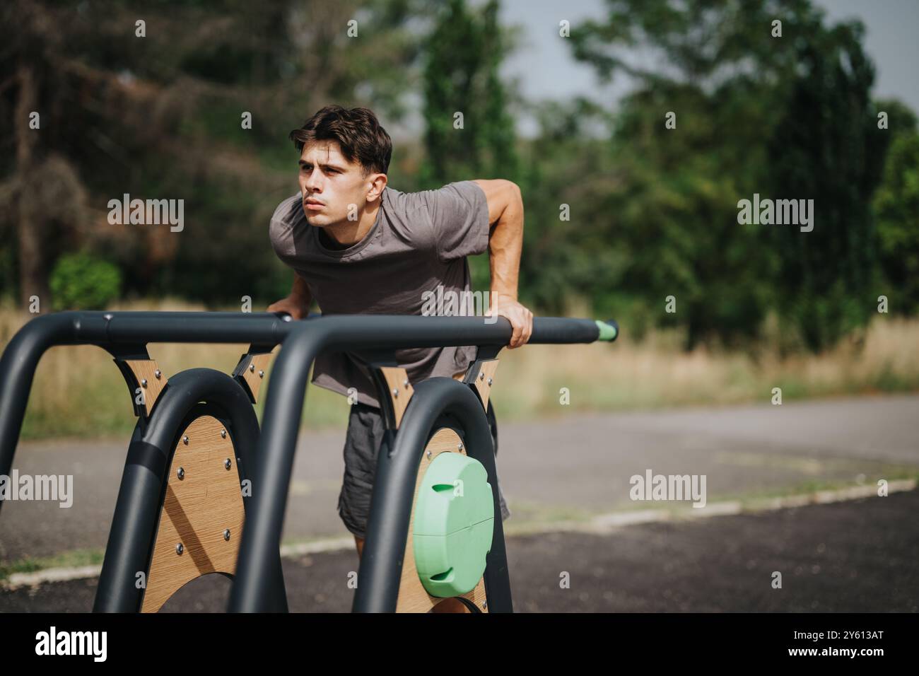 Man working out triceps by doing dips on outdoor gym equipment in the park, emphasizing physical fitness, health, and wellness in a natural setting. Stock Photo