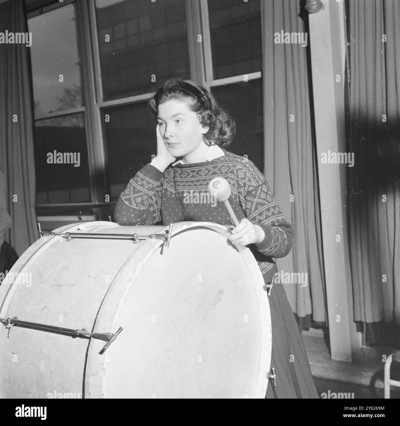 LONDON 19 YEAR OLD MARGARET CONWAY FROM BRIXTON IN LONDON IS CAUGHT IN A MOMENT BETWEEN THE OVERTURES AND TAKES IT EASY ON HER BIG BASS DRUM WHILE WAITING FOR THE TAP OF THE CONDUCTORS BATON.  QUINTIN SCHOOL IN ST JOHNS WOOD IN LONDON STARTS AN CHRISTMAS COURSE BY THE LONDON SCHOOLS SYMPHONH ORCHESTRA IN PREPARATION FOR THEIR 18 JANUARY CONCERT AT THE ROYAL FESTIVAL HALL.  28 DECEMBER 1959 Stock Photo