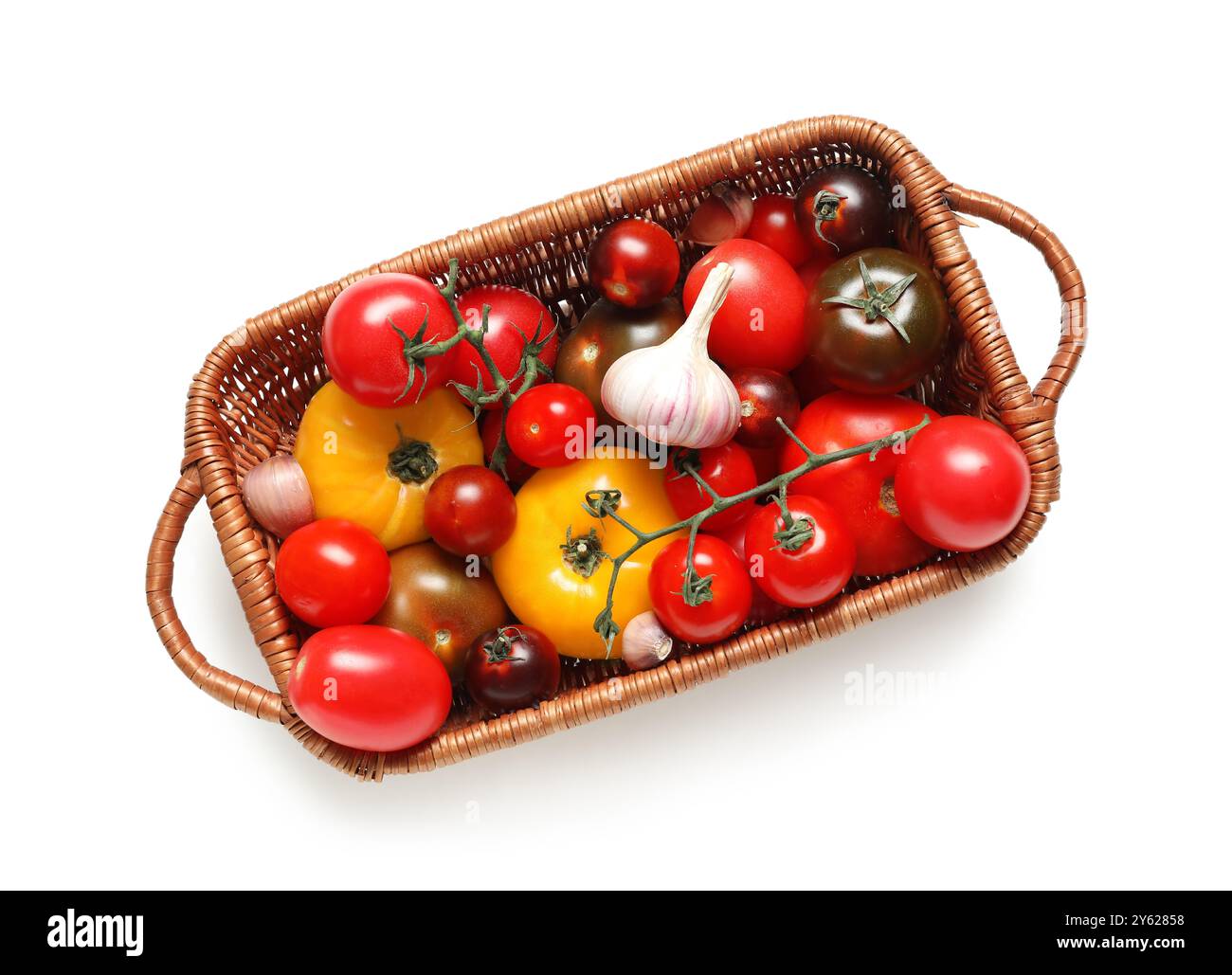 Wicker basket with different fresh tomatoes and garlic on white ...