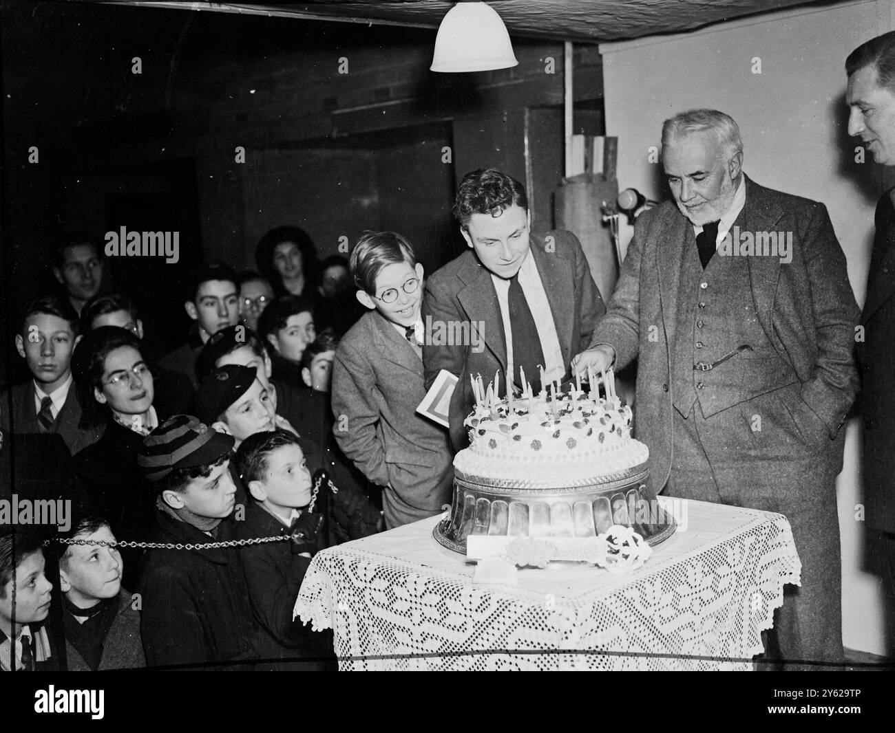 Prof C.E.M.'Brains Trust' Joad, declared the 1948 21st Schoolboy's Own Exhibition opened today at the Royal Horticultural Hall. He also cut the giant 21st birthday cake under the critical eye of William (Billy Nelson Jr) and Ginger (Maxwell Longmuir) stars of their 'Just William' stage and radio show. Picture shows: watched by 'William' and 'Ginger' (glasses) Prof Joad carefully cuts the 21st birthday cake at the exhibition today.  1 January 1948 Stock Photo