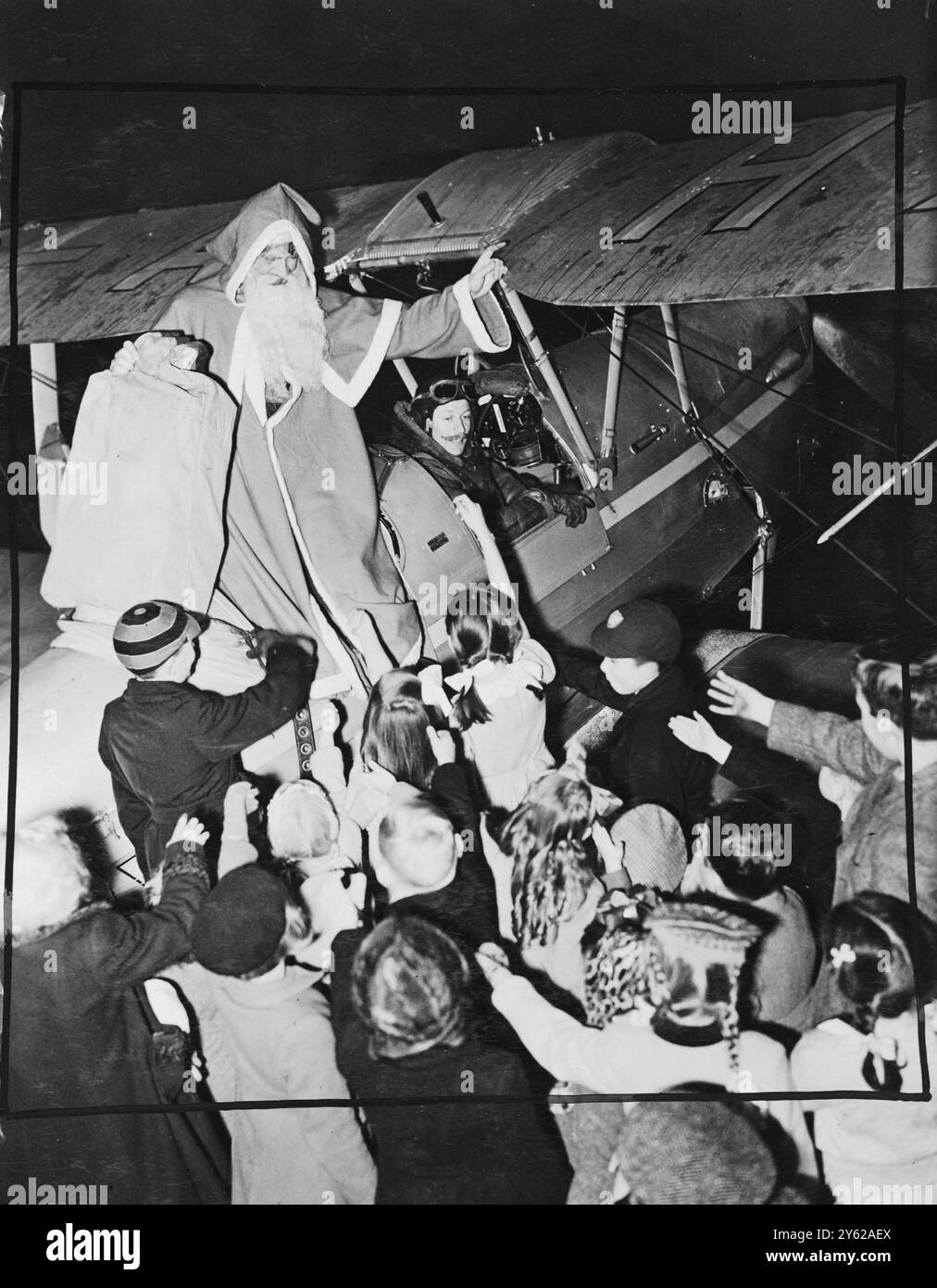 A seasonable V.I.P. dropped in No.22 Reserve Flying School Cambridge, today when Santa Claus arrived by air to distribute presents to the air-minded youngsters of officers and airmen attending the Annual Christmas party. Picture Shows: 'Santa touches down' - Father Christmas, (F/Lt. Semple, Adjutant, No. 5 Reserve) is welcomed by eager children.  20 December 1947 Stock Photo