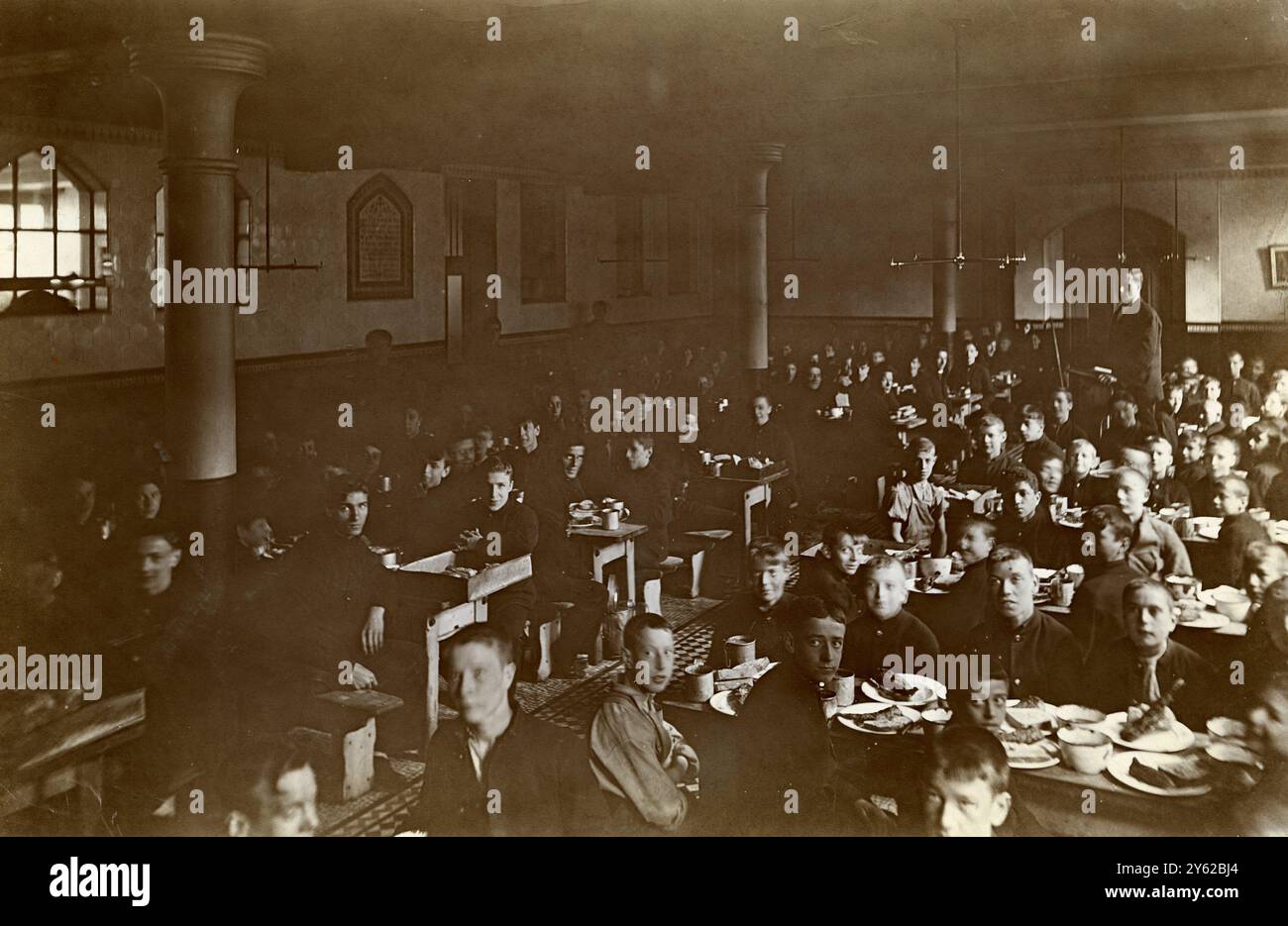 ARCHIVE BOX 3 ARC 0085   D589  Reference: 001386   THE REFRECTORY AT STEPNEY BOYS HOME        DATE : 1910    DINNER / EATING / MEAL                                  BOYS SITTING AT LONG TABLES : ENAMEL PLATES : CHIPPED ENAMEL BOWLS : BREAD AND HERRINGS TO EAT. Stock Photo