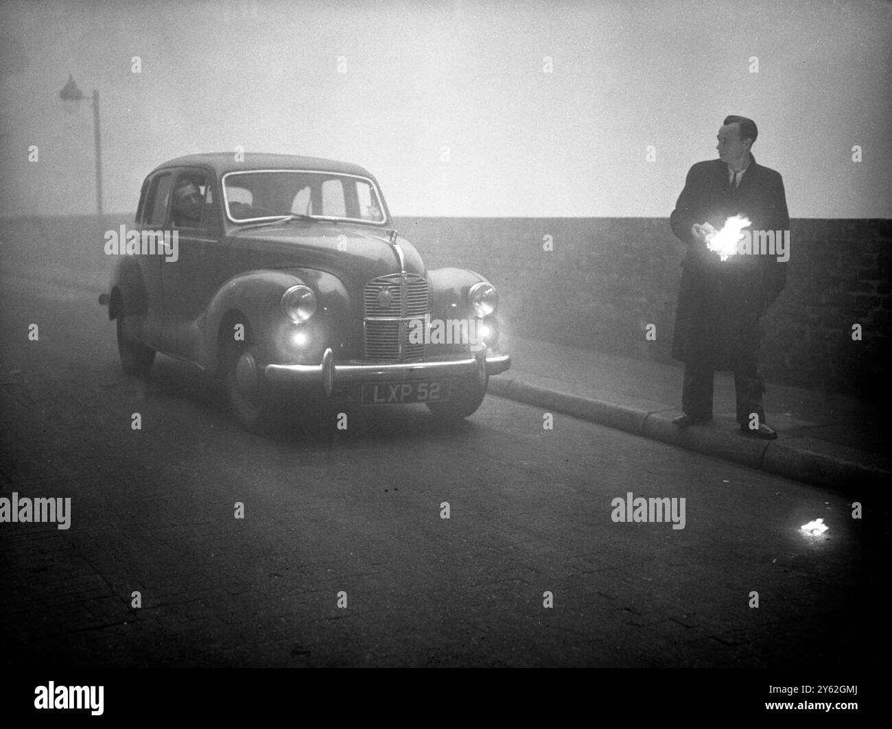 Traffic chaos in the fog London blacked out - A blanket of fog which covered London , brought road and rail traffic to a crawl and halted ships and planes .  Many passengers in public vehicles and private cars helped the drivers along on their journey by walking in front of the vehicles with lighted torches or lighted beacons .  Photo shows:  A pedestrian helps a motorist along by holding a lighted beacon to show him on his way , picture taken in the City of London today  6 December 1952 Stock Photo