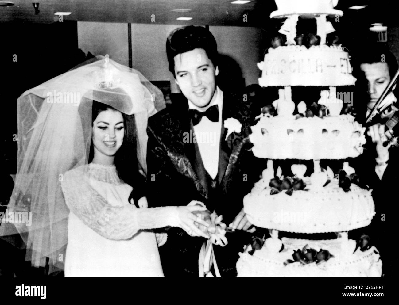 First millionaire rock 'n' roll singer Elvis Presley helps his bride 22-year-old Priscilla Ann Beaulieu to cut their wedding cake at a reception which followed their wedding, at Alladin Hotel here today 1st May. 32-year-old Presley and Miss Beaulieu first met in 1959 during his army stint in germany where her father was an air force officer. The wedding ceremony took place in the home of hotel owner Milton Prell. It was Presley's first marriage - 1st May 1967 Stock Photo