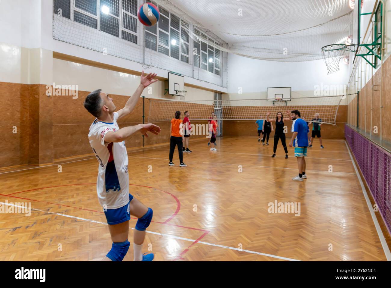 Mature man serving the ball in volleyball. Friends playing volleyball. Sport  game with group of people indoor. Belgrade, Serbia - May 10. 2024. Stock Photo