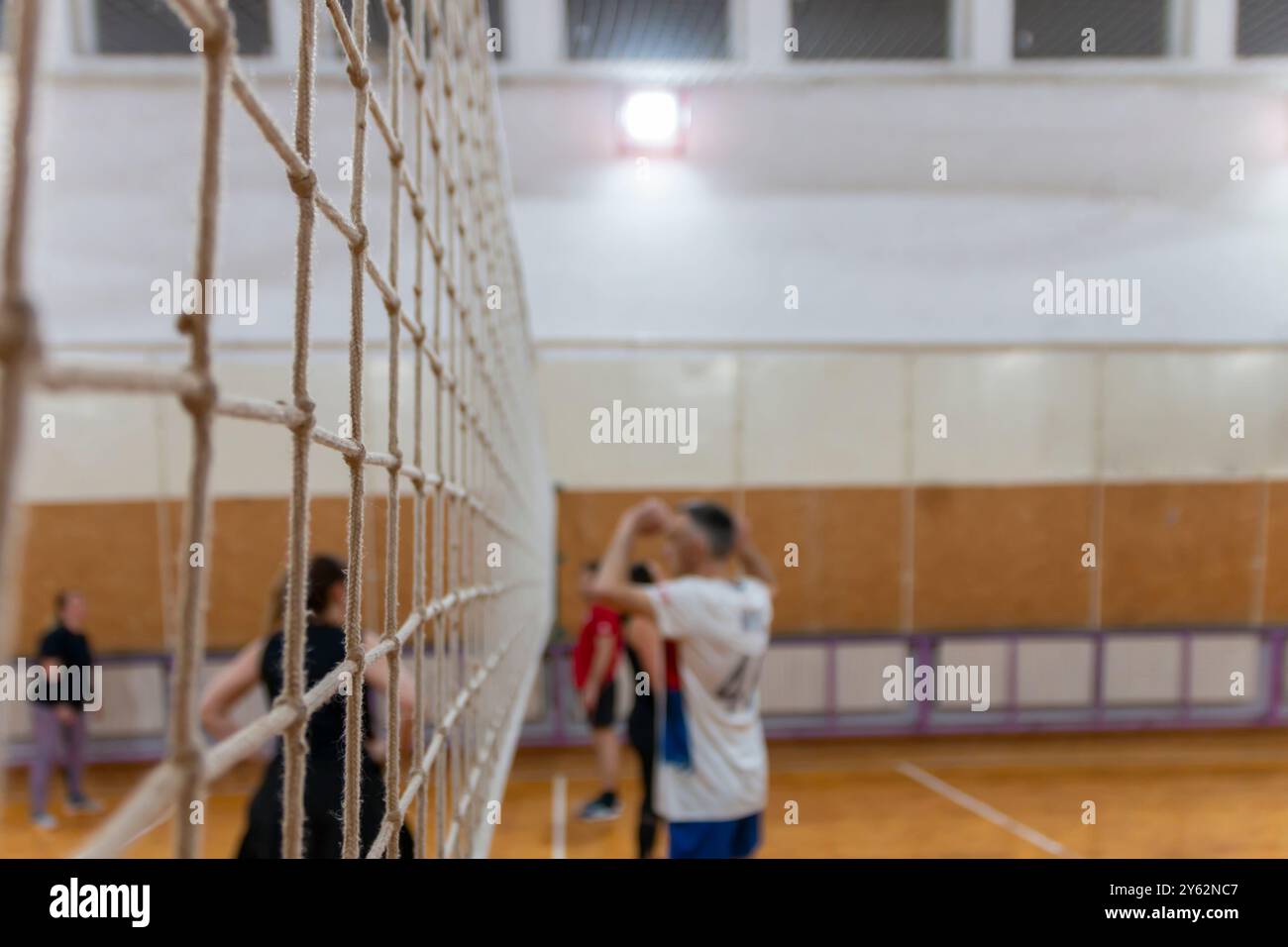 A volleyball net stretched at indoor court. A volleyball court with people around with volleyball net stretched on it. Stock Photo