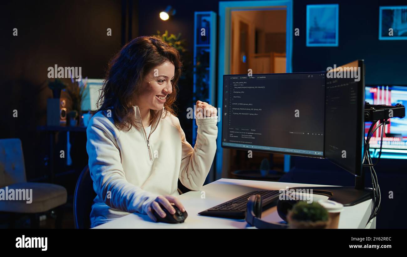 Joyous woman doing software quality assurance celebrating after reading source code and finding no errors. Cheerful engineer excited after inspecting coding on desktop PC, seeing no issues, camera B Stock Photo