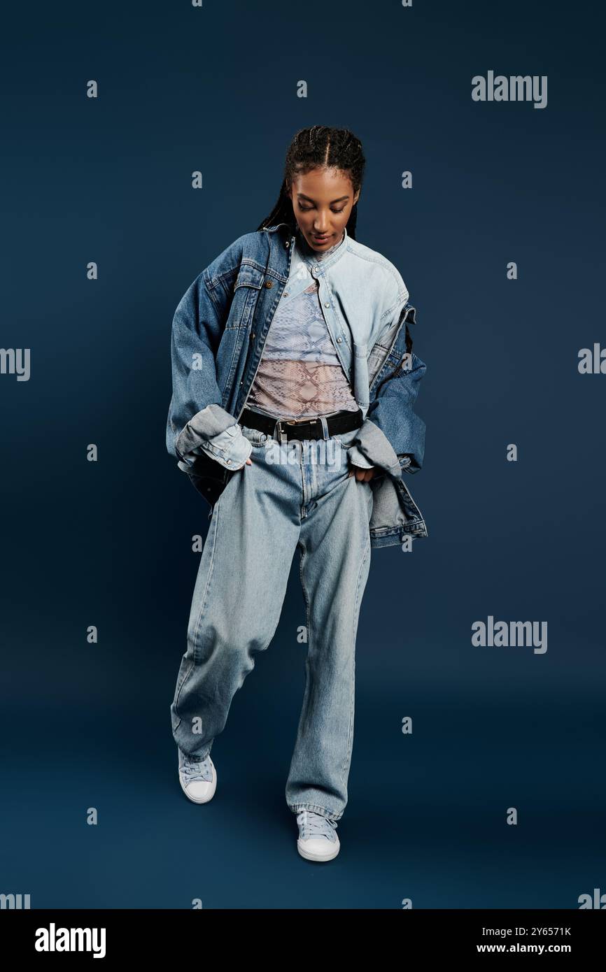 A stylish young woman confidently poses in relaxed denim against a blue ...