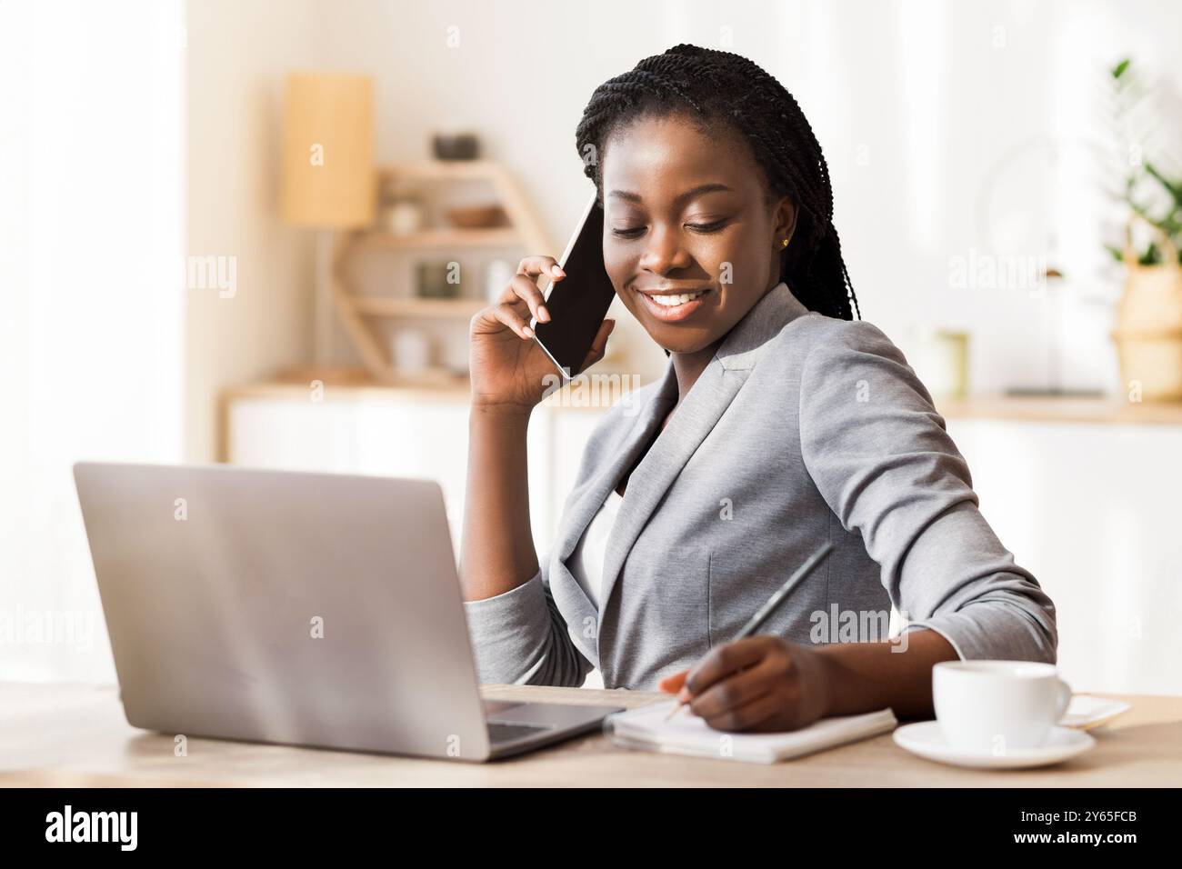 Afro Businesswoman Taking Notes While Having Phone Conversation In Modern Office Stock Photo