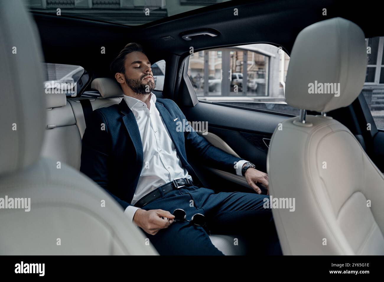 Feeling overworked. Tired young man in full suit keeping eyes closed ...