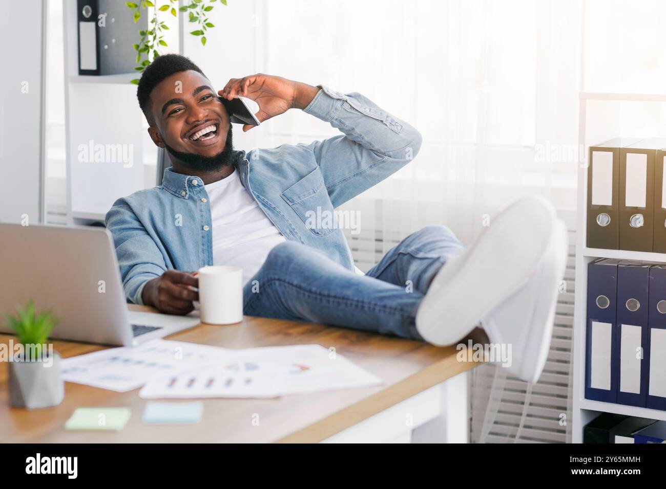 Joyful black manager talking on phone while having break at work Stock Photo