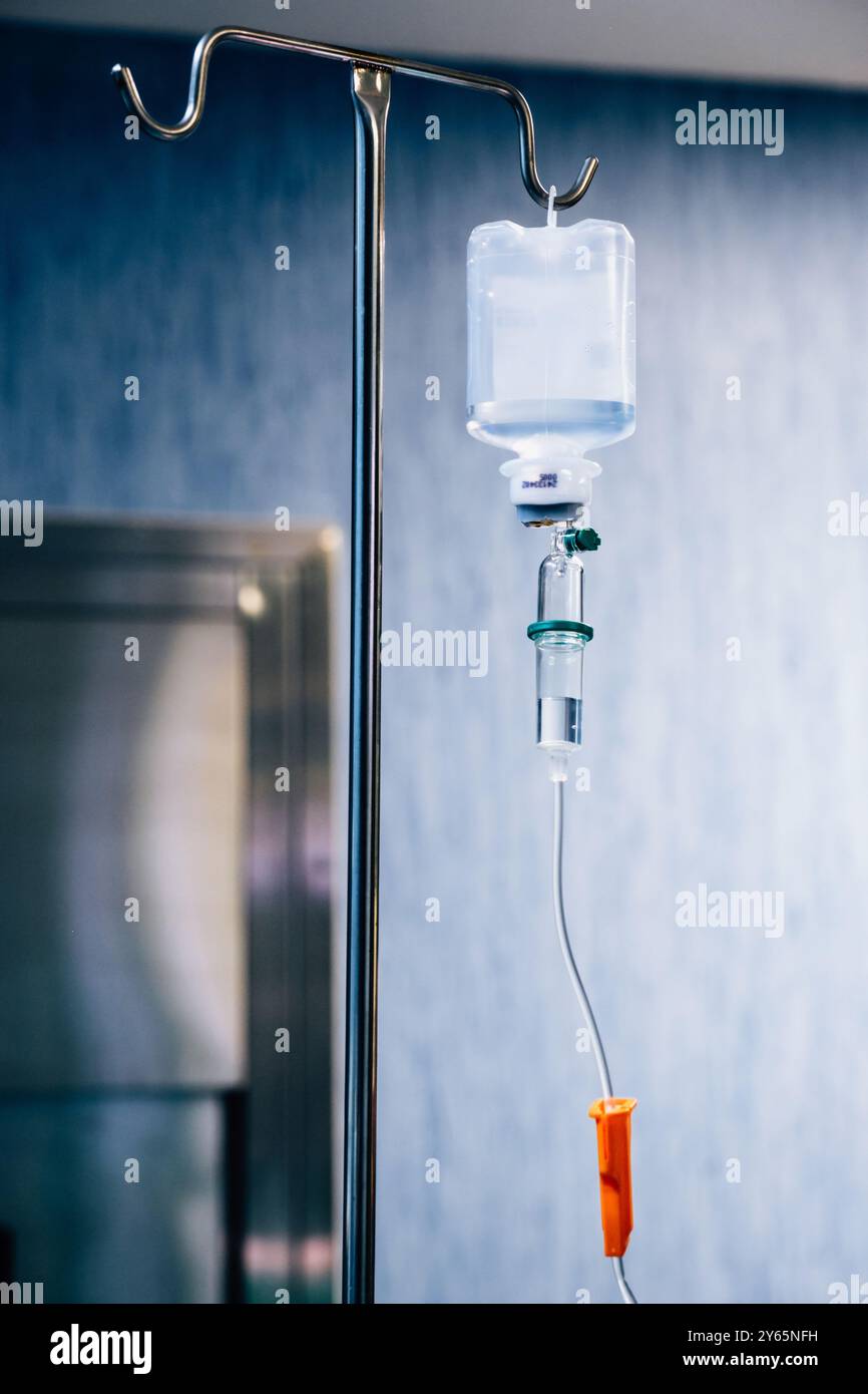 Close-up of an IV drip against a blue hospital wall, highlighting the ...