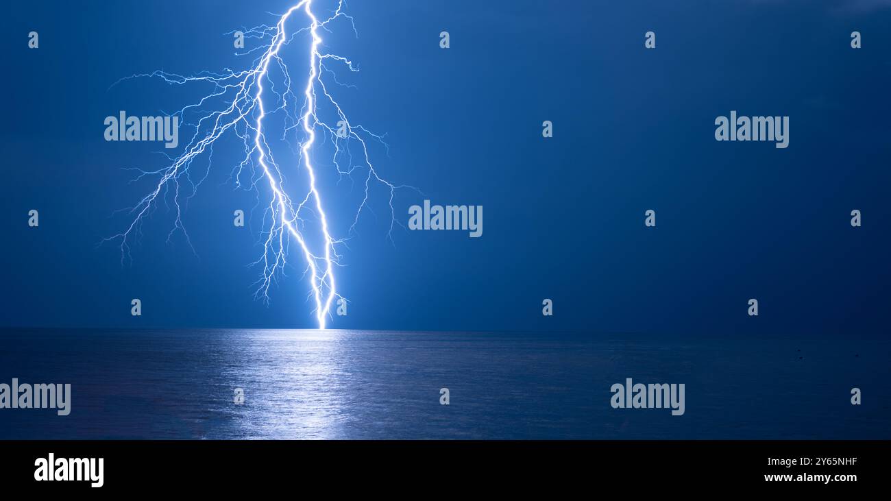 A dramatic and powerful lightning strike illuminates the dark sky over ...