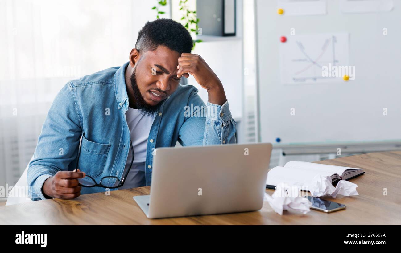 Stressed african worker looking to laptop screen with despair Stock Photo