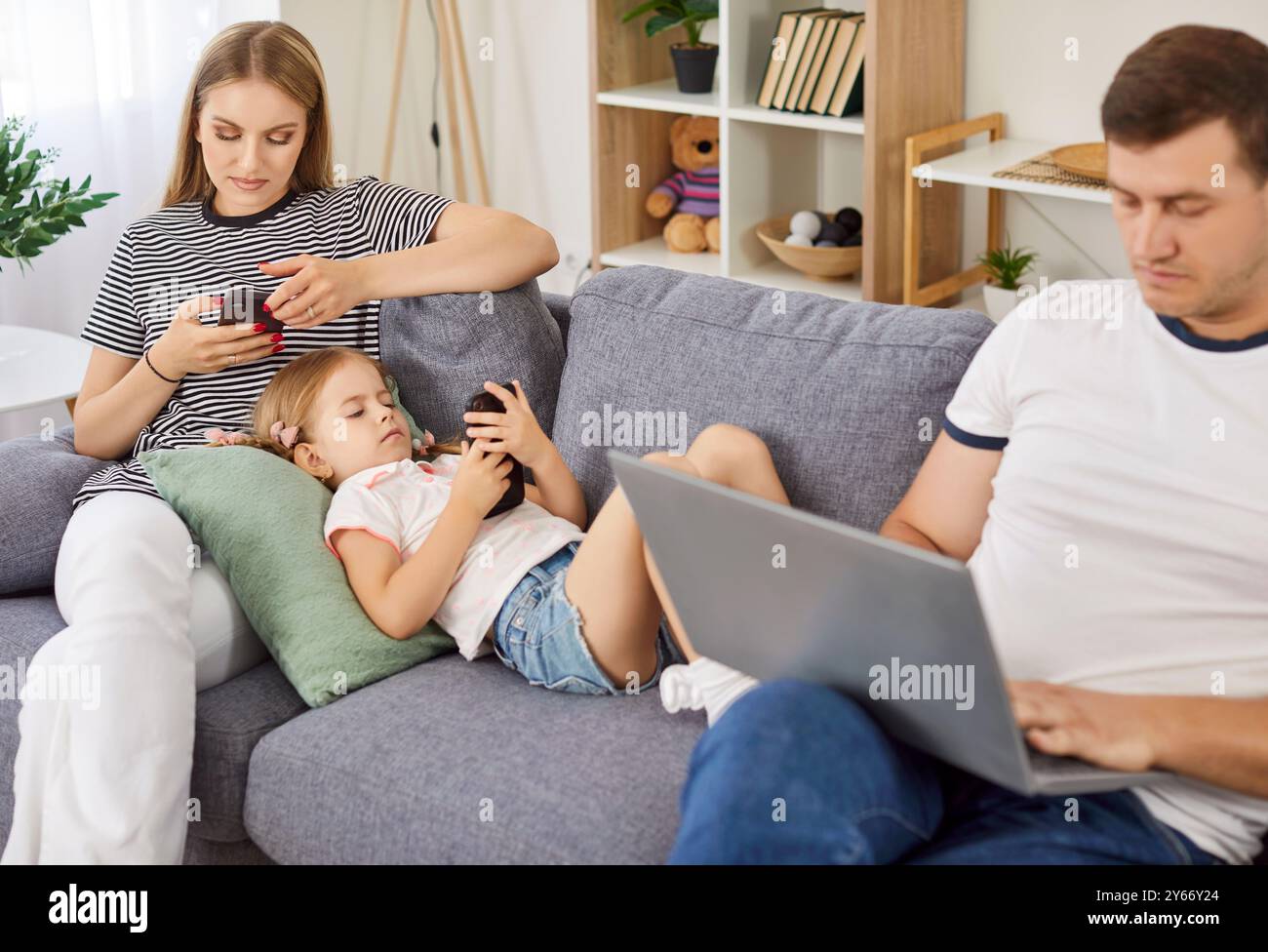 Family at home using laptop and smartphones sitting on sofa, entertaining online obsessed  Stock Photo